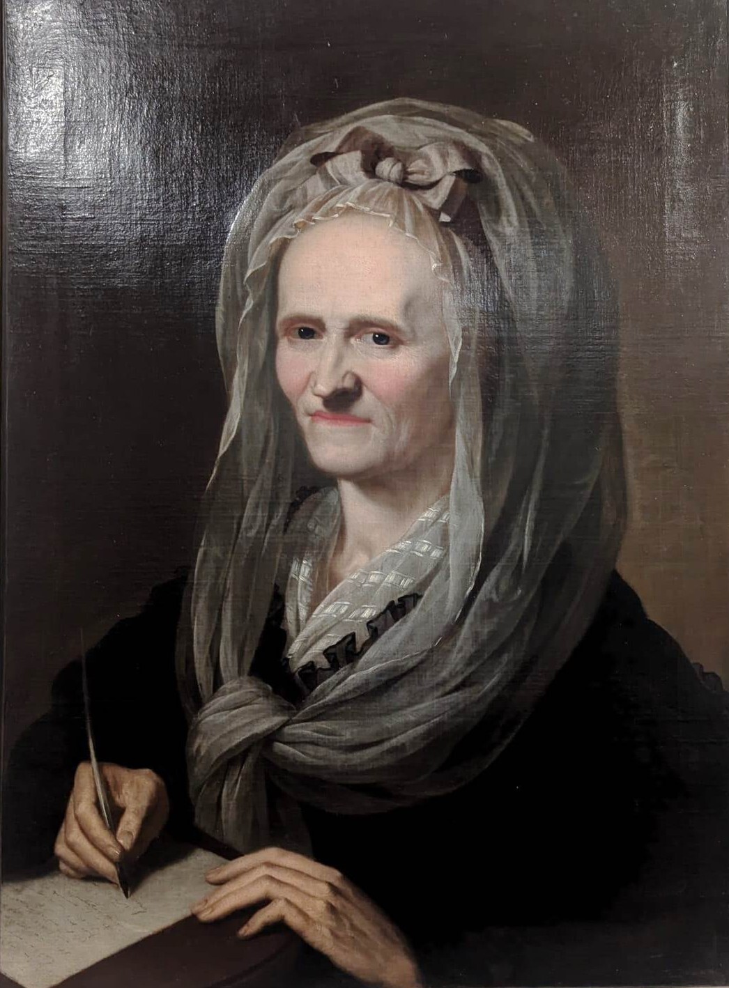 Das Gemälde zeigt ein Portrait von Anna Louisa Karsch als ältere Frau. Sie trägt eine Haube mit Schleife unter einem grauen Tuch, das sie vor der Brust leicht zusammengeknotet hat. Darunter trägt sie ein schwarzes langes Kleid.