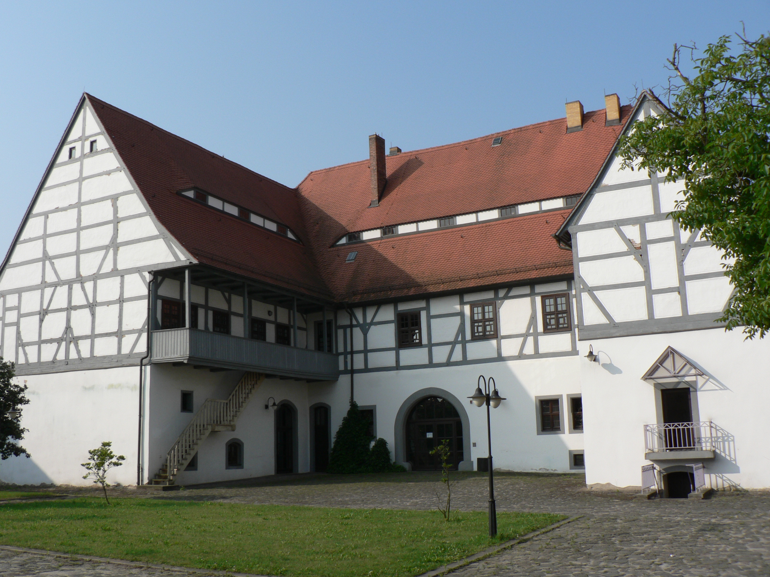 Der Hintereingang des Amtshauses. Ein weißes Fachwerkhaus mit grauen Balken steht hinter einer grünen Wiese.