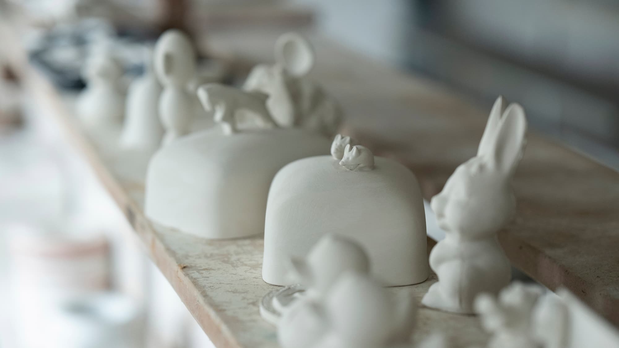Weiße Rohlinge aus der Schauproduktion. Ein Hase und eine Butterglocke mit zwei kleinen Mäusen stehen auf einem Regal zum Trocknen.