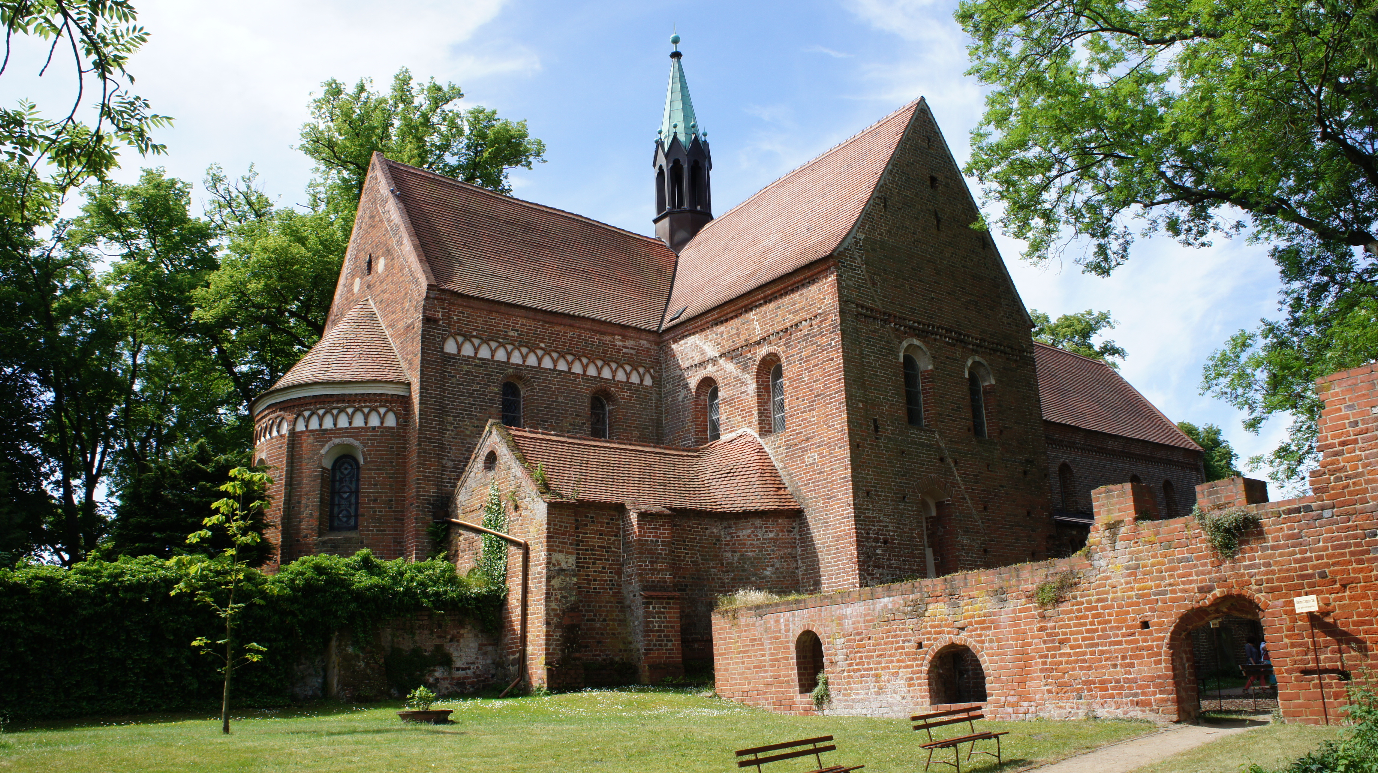 Die nordöstliche Außenfassade von Kloster Arendsee. Vor dem romanischen Backsteinbau befindet sich eine Wiese und eine Backsteinmauer.
