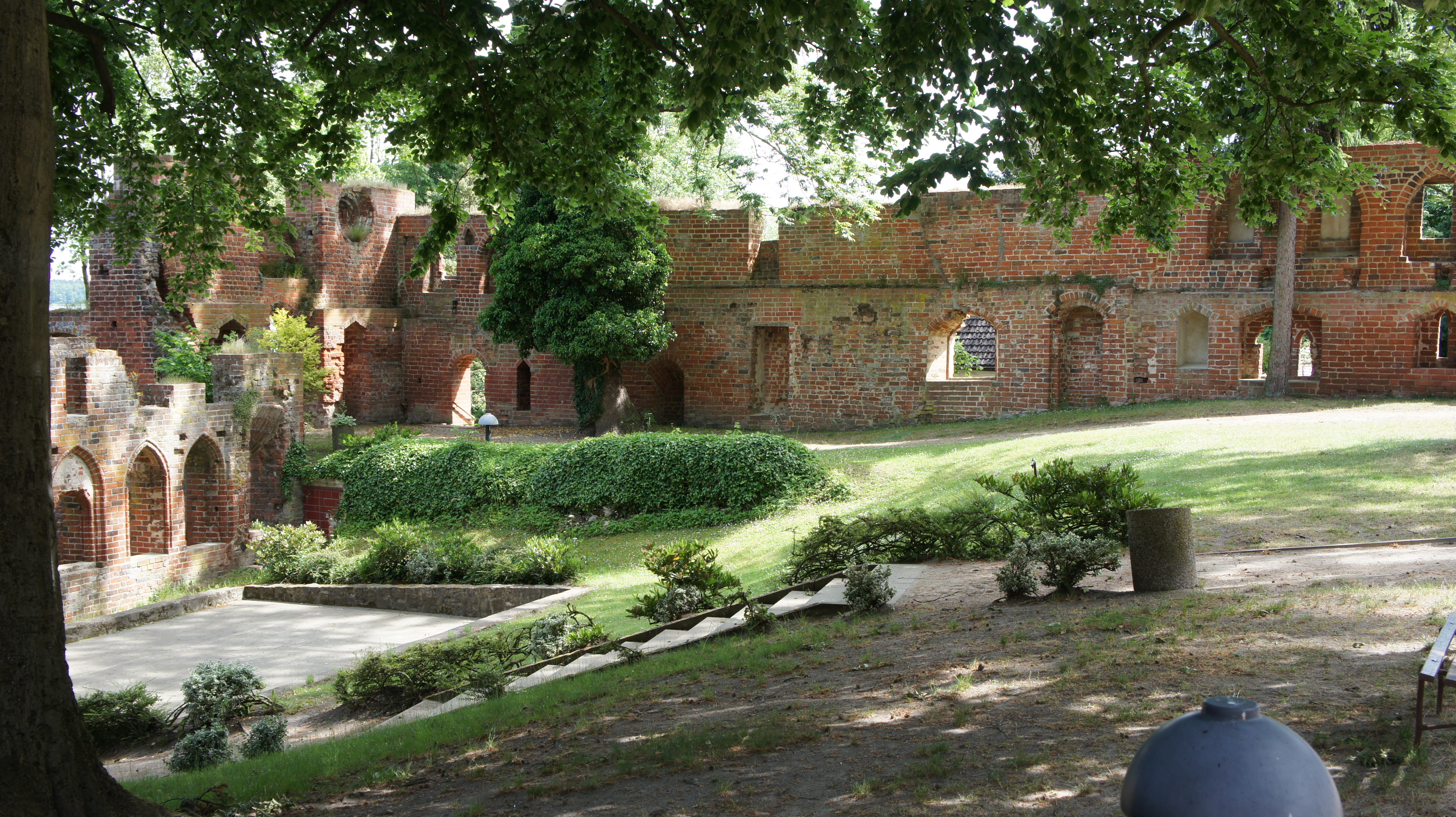 Die teilweise noch erhaltenen Klostermauern aus rotem Backstein umgeben eine grüne Parkanlage aus Bäumen und Hecken.
