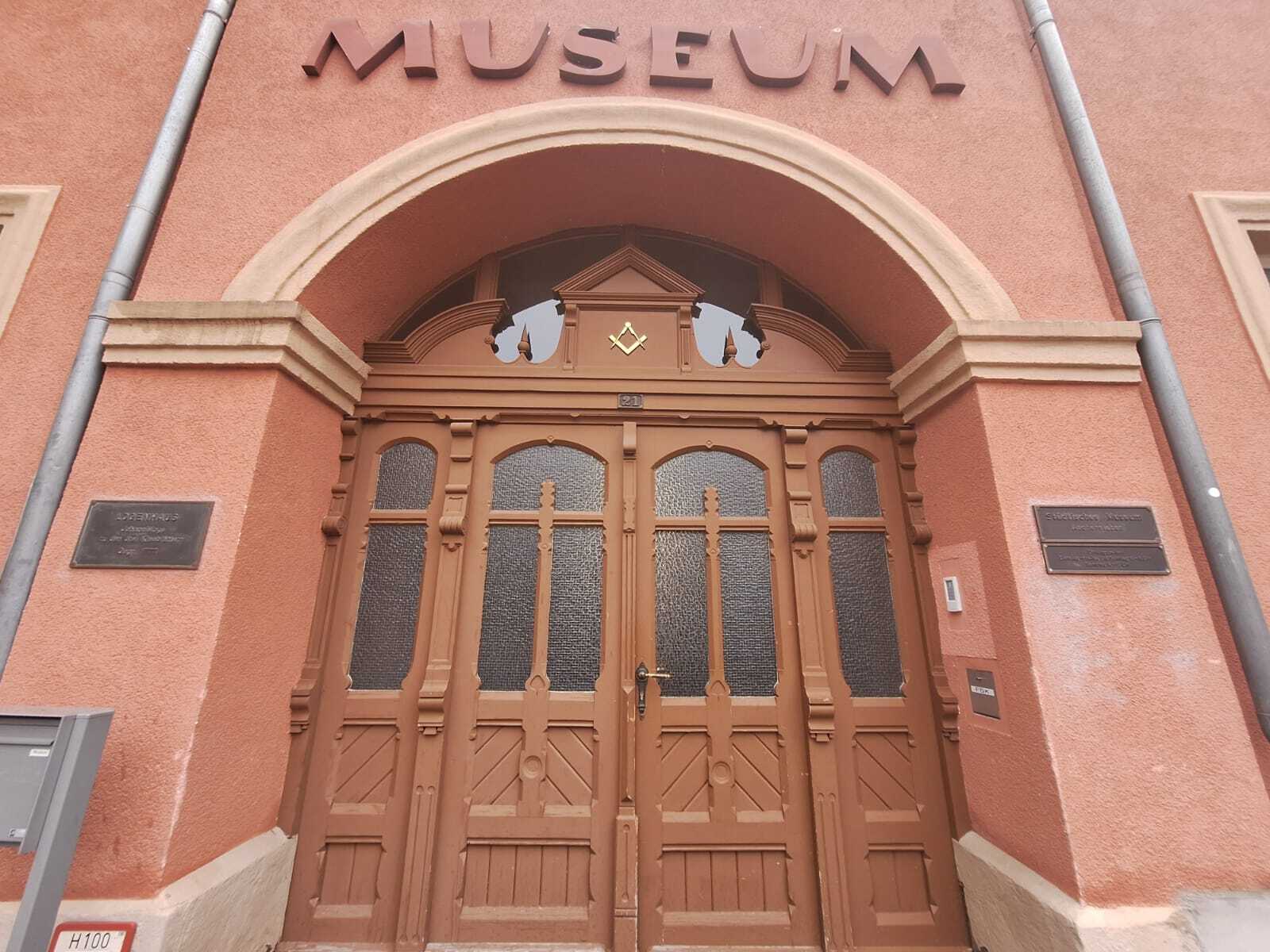 Eingang zum Museum Aschersleben. Eine große braune Holztür mit Fenstern führt in das Innere des Museums. Die Fassade ist in einem Terrakotta gestrichen.