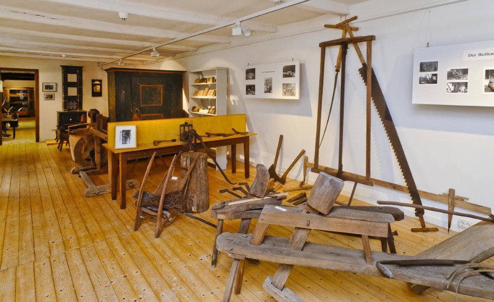 Abteilung der Volkskunde. Landwirtschaftliche Geräte werden in einem Ausstellungsraum präsentiert. An den Wänden hängen Tafeln mit Bildern zur Nutzung der Geräte.
