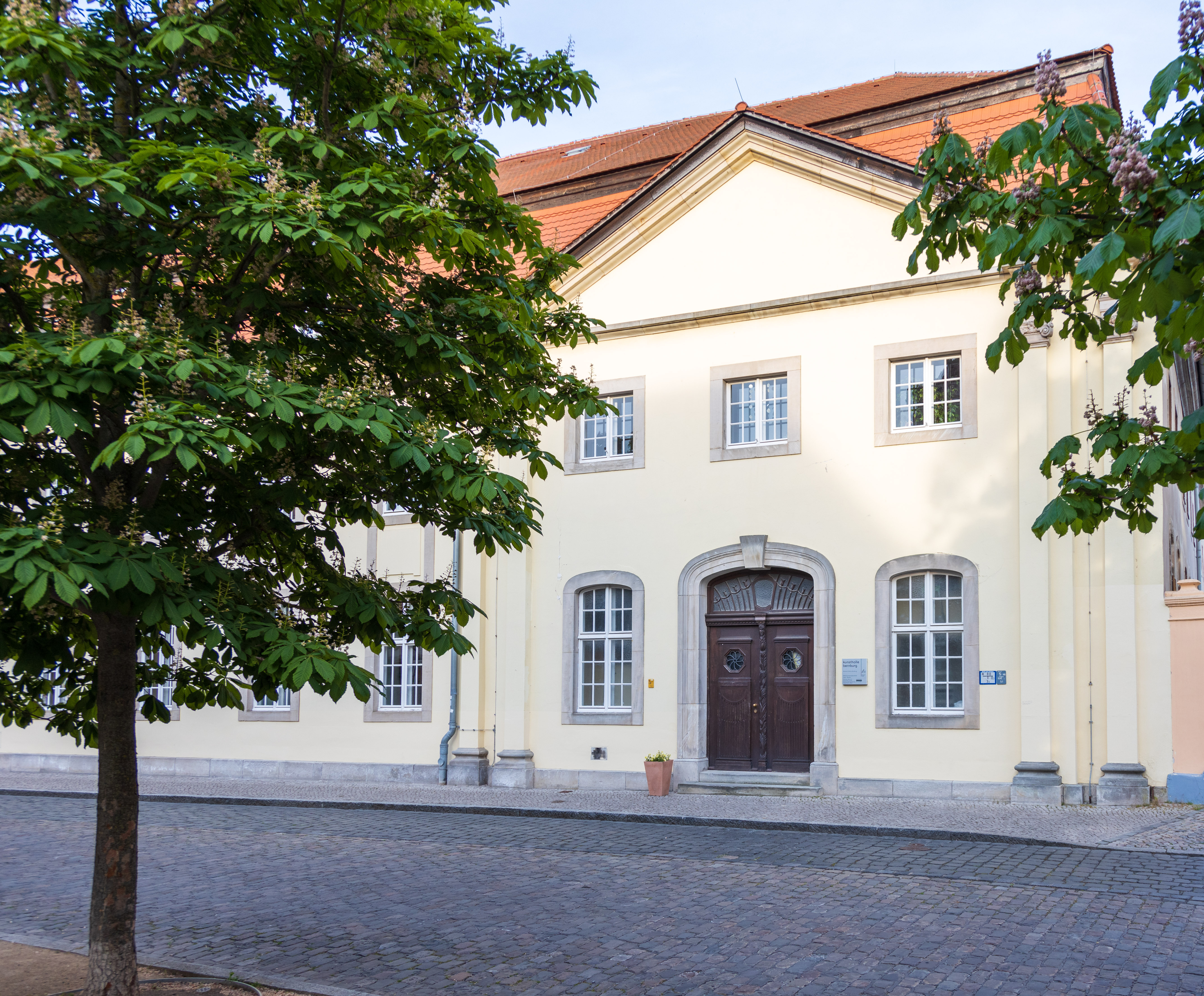 Kunsthalle Bernburg, Außenansicht. Eine gelbe Fassade mit einem Dreiecksgiebel und einer braunen massiven Holztür.