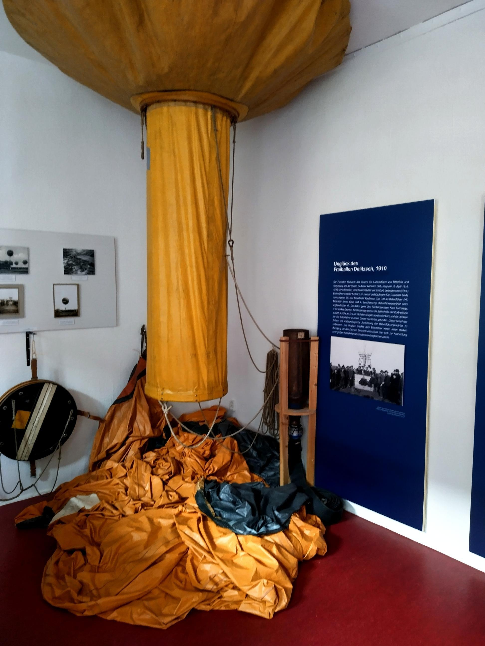 Bitterfelder Ballonfahrt Ausstellung. Der obere Teil eines gelben Heißluftballons hängt neben einer blauen Informationstafel.