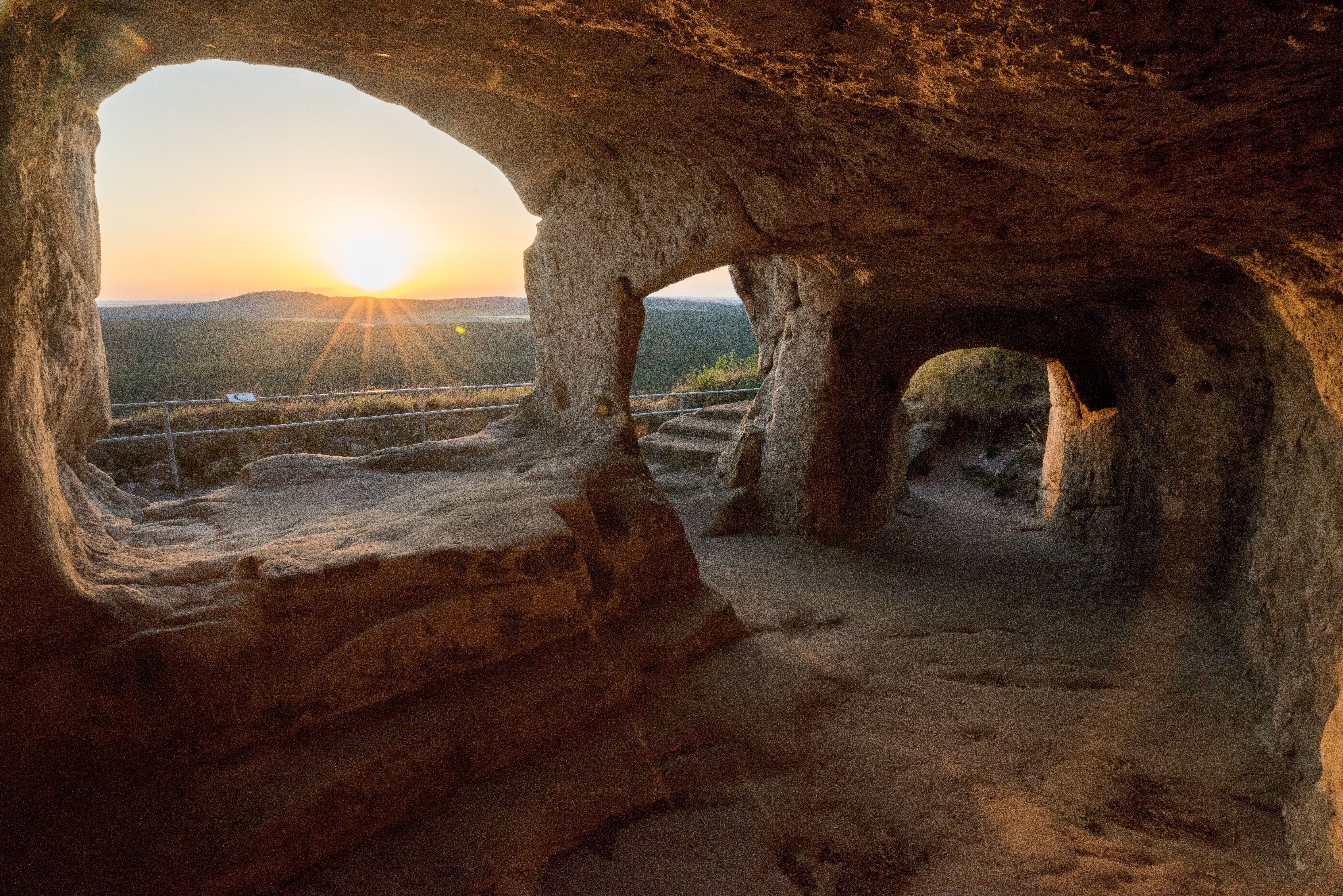 Ausblick aus einer Felsenhöhle auf den Wald und Sonnenaufgang.