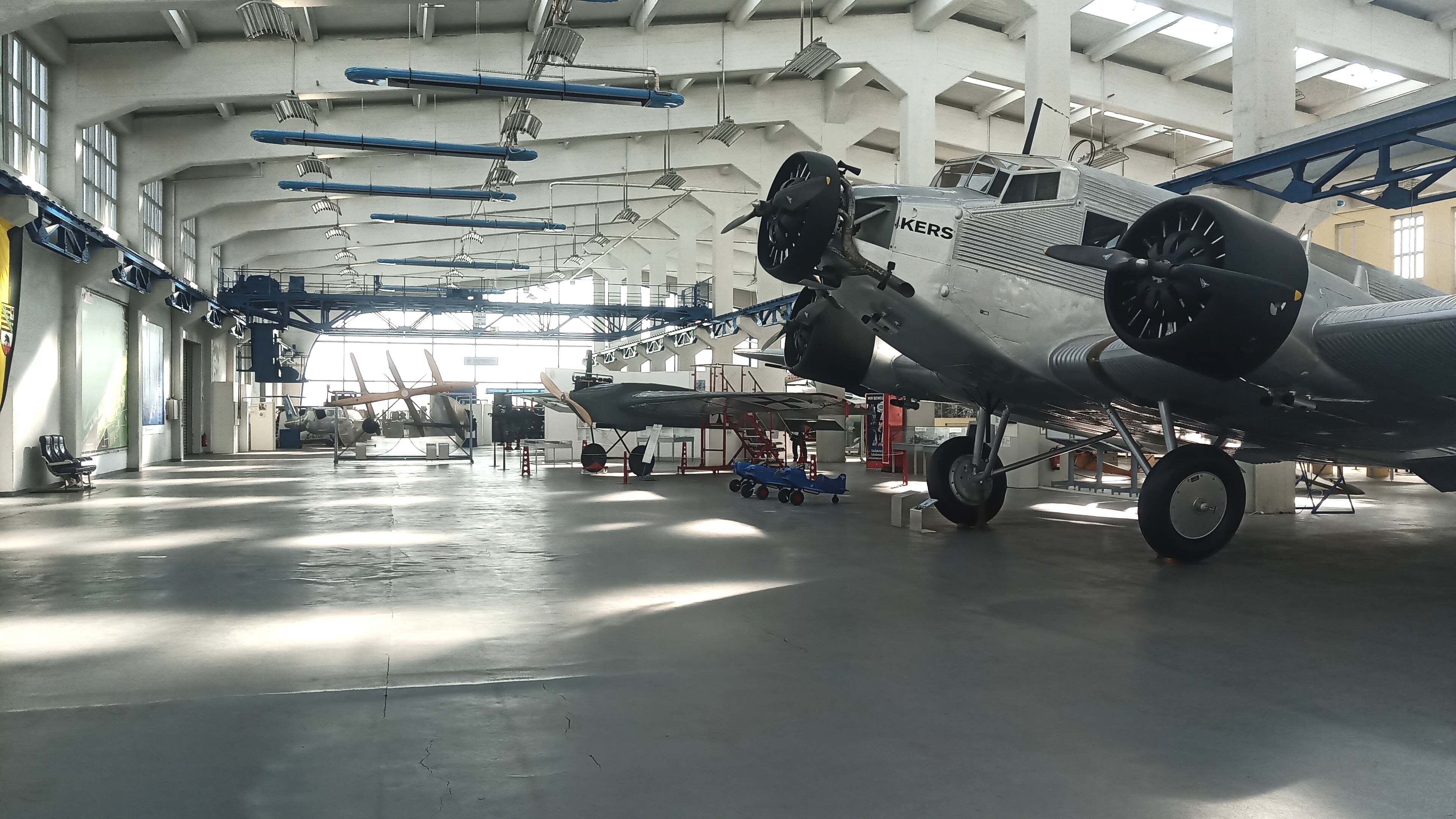 In der Museumshalle sind mehrere kleine silberne Flugzeuge nebeneinander aufgestellt. Die Halle ist große und hell.