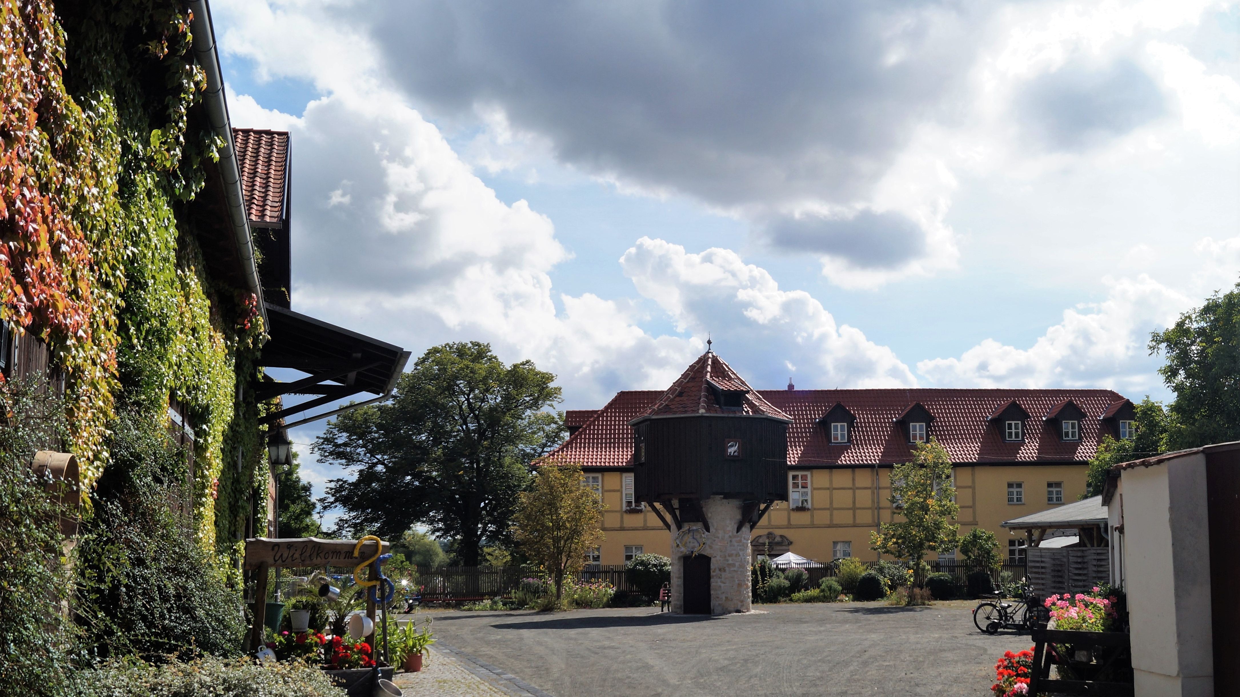 Hof des Heimatvereins und Museum. In der Mitte des Hofes steht ein Taubenschlag aus Holz. Dahinter befindet sich ein großes gelbes Gebäude. Auf der linken Seite sind Weinranken an einem Haus im Hof erkennbar.