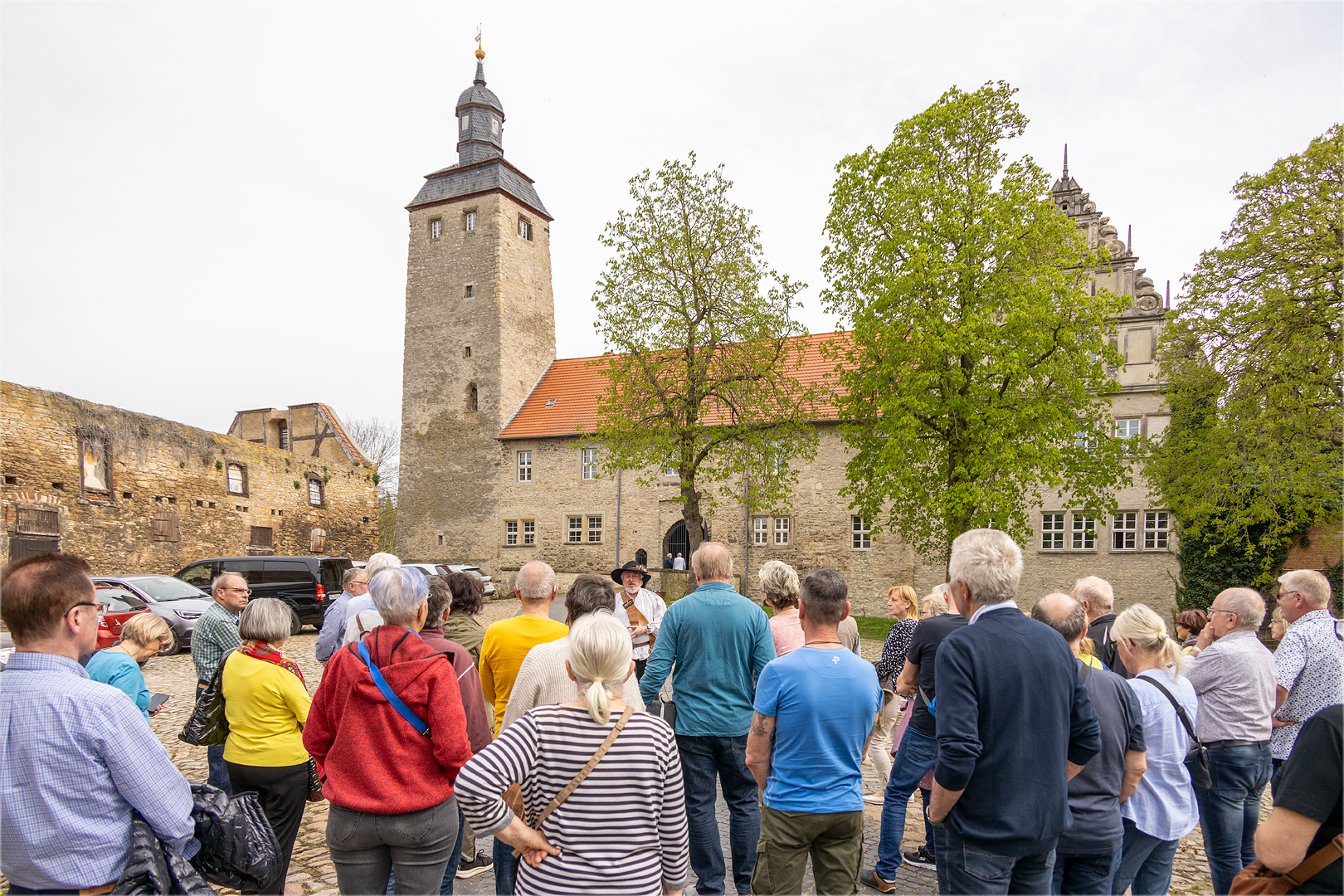 Führung auf der Wasserburg Egeln. eine Gruppe von Menschen steht vor der Burganlage. Auf der linken Seite befindet sich eine Ruine ohne Dach, daneben der Bergfried und die anschließende Burganlage.
