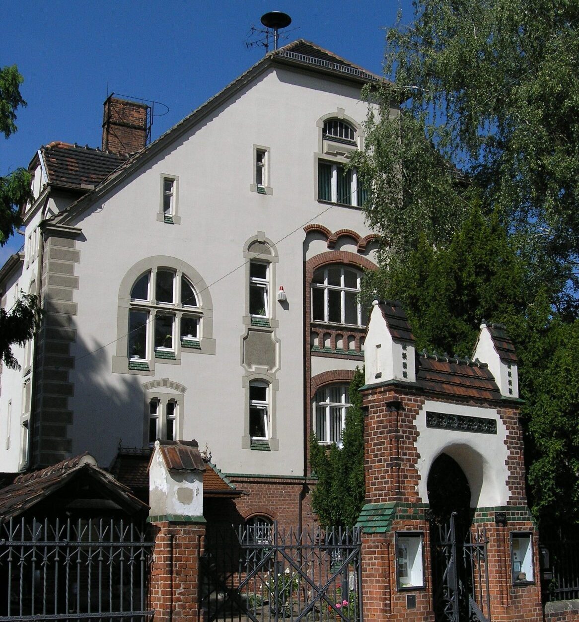 Genthin Kreismuseum. Eine Villa mit einer weißen Außenfassade und Backsteinelemente. Ein Tor aus Backstein dient als Zugang zum Museum.
