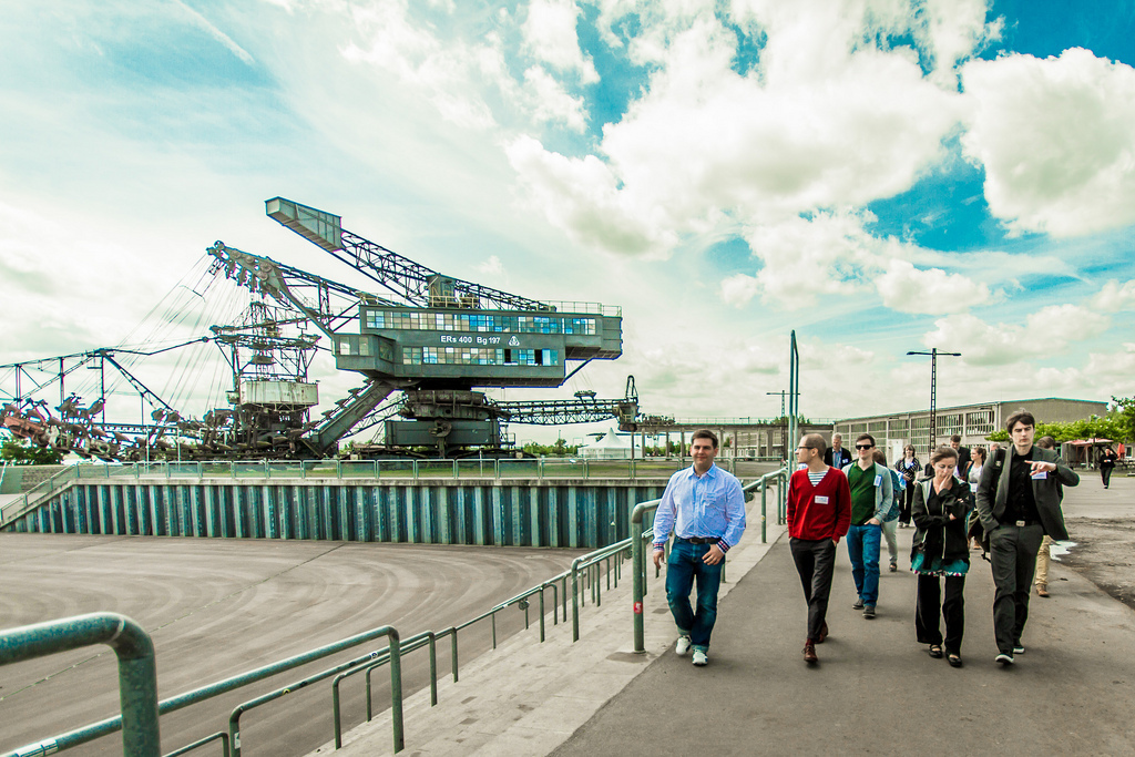 Führung auf Ferropolis. Eine Gruppe wird über das Gelände von Ferropolis geführt. Im Hintergrund stehen riesige Braunkohle-Bagger.