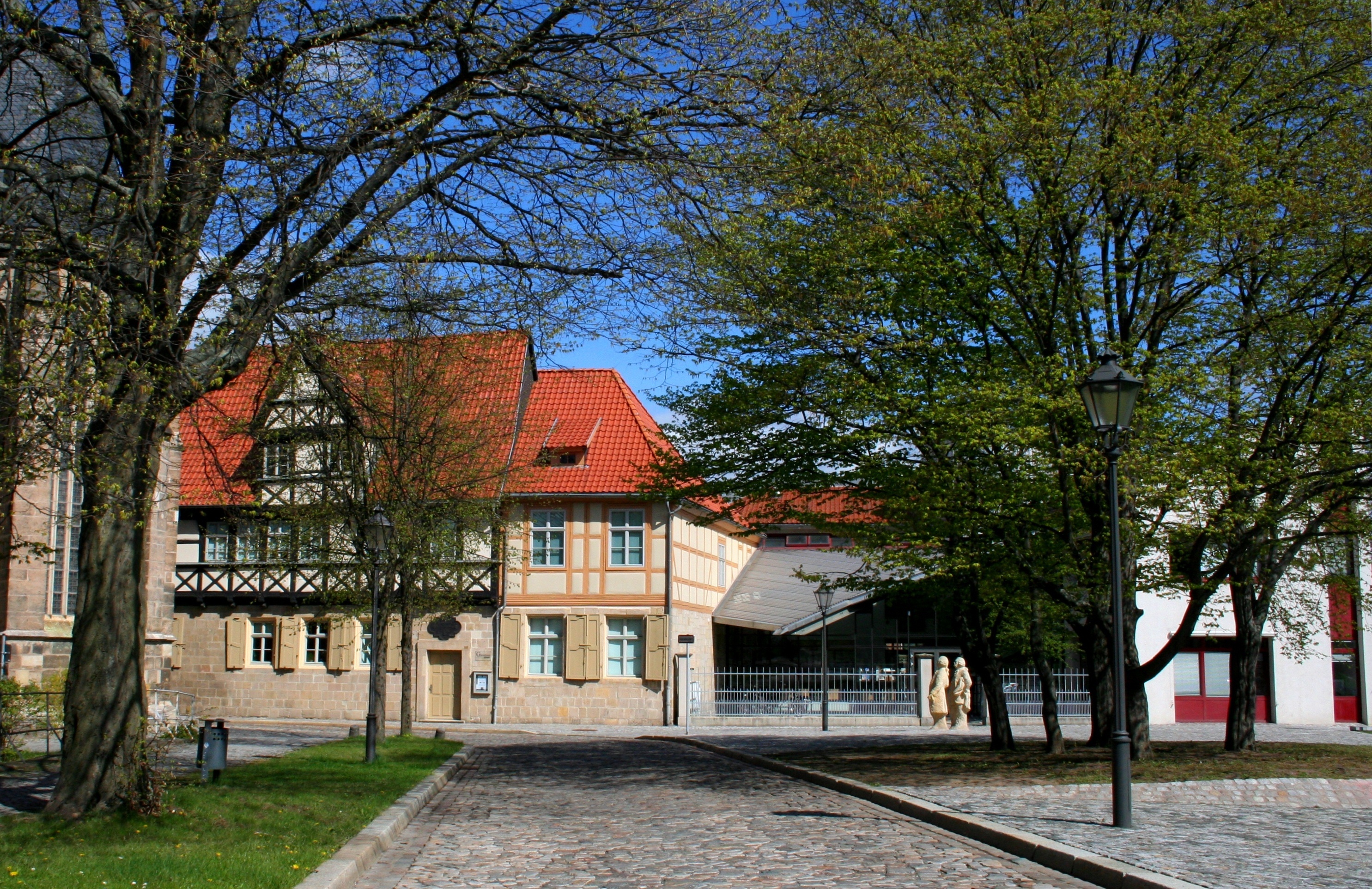 Das Gleimhaus von Außen. Hinter mehreren Bäumen schauen zwei Fachwerkfassaden hervor. Eines der Häuser hat dunkles und das andere helles Fachwerk. Beide besitzen ein rotes Ziegeldach. Daneben ragt ein abknickendes Vordach hervor.