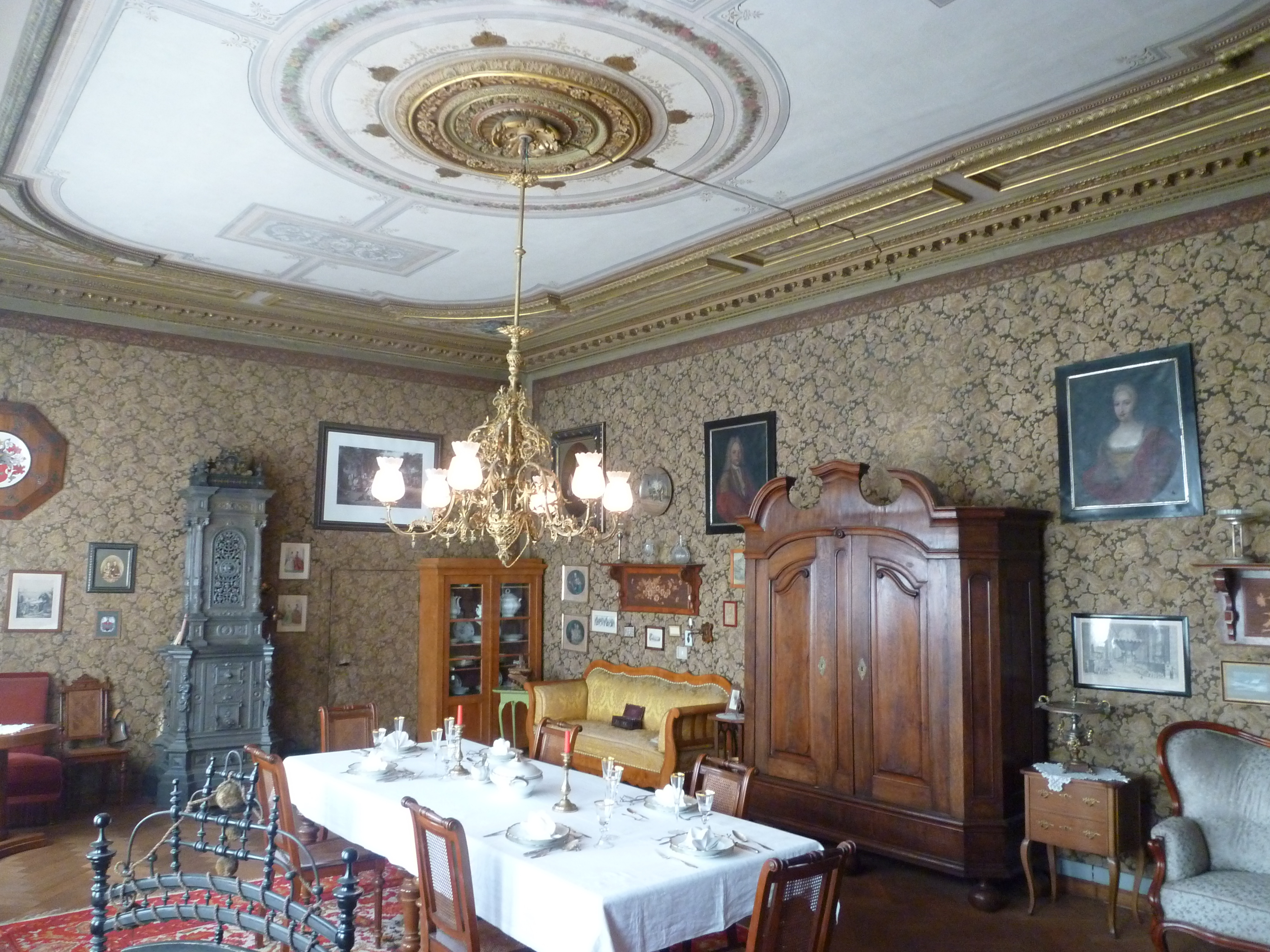 Im bürgerlichen Salon des Schraubemuseums steht ein großer Tisch in der Mitte des Raumes. An den Seiten stehen Schränken und edel bezogene Sofas. Von der Stuckdecke hängt ein goldener Kronleuchter.