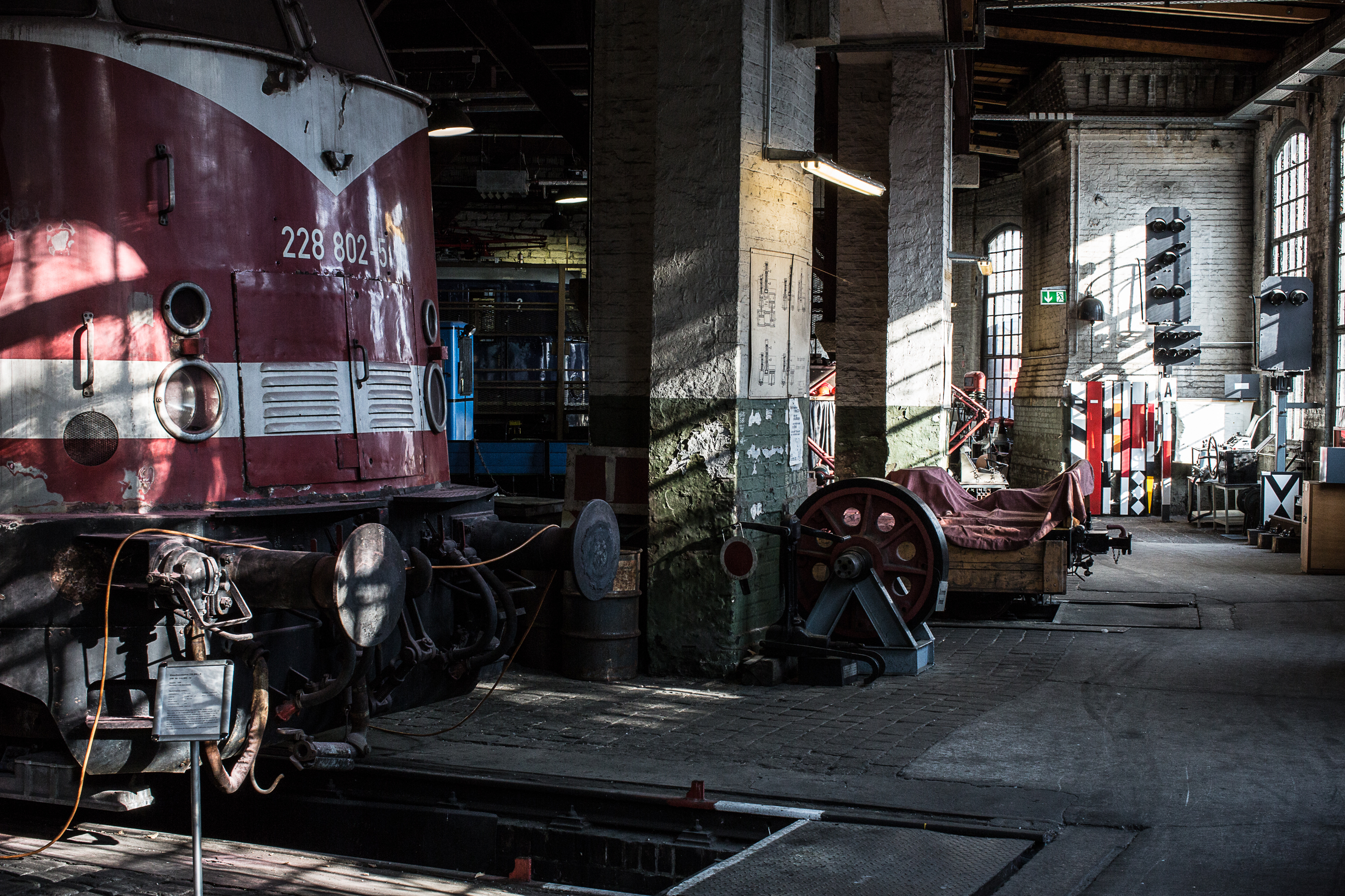 Eine dunkelrote Bahn mit einem weißen Streifen steht im Schuppen. Im Hintergrund befinden sich Werkzeuge, Technik und weitere Bahnen.