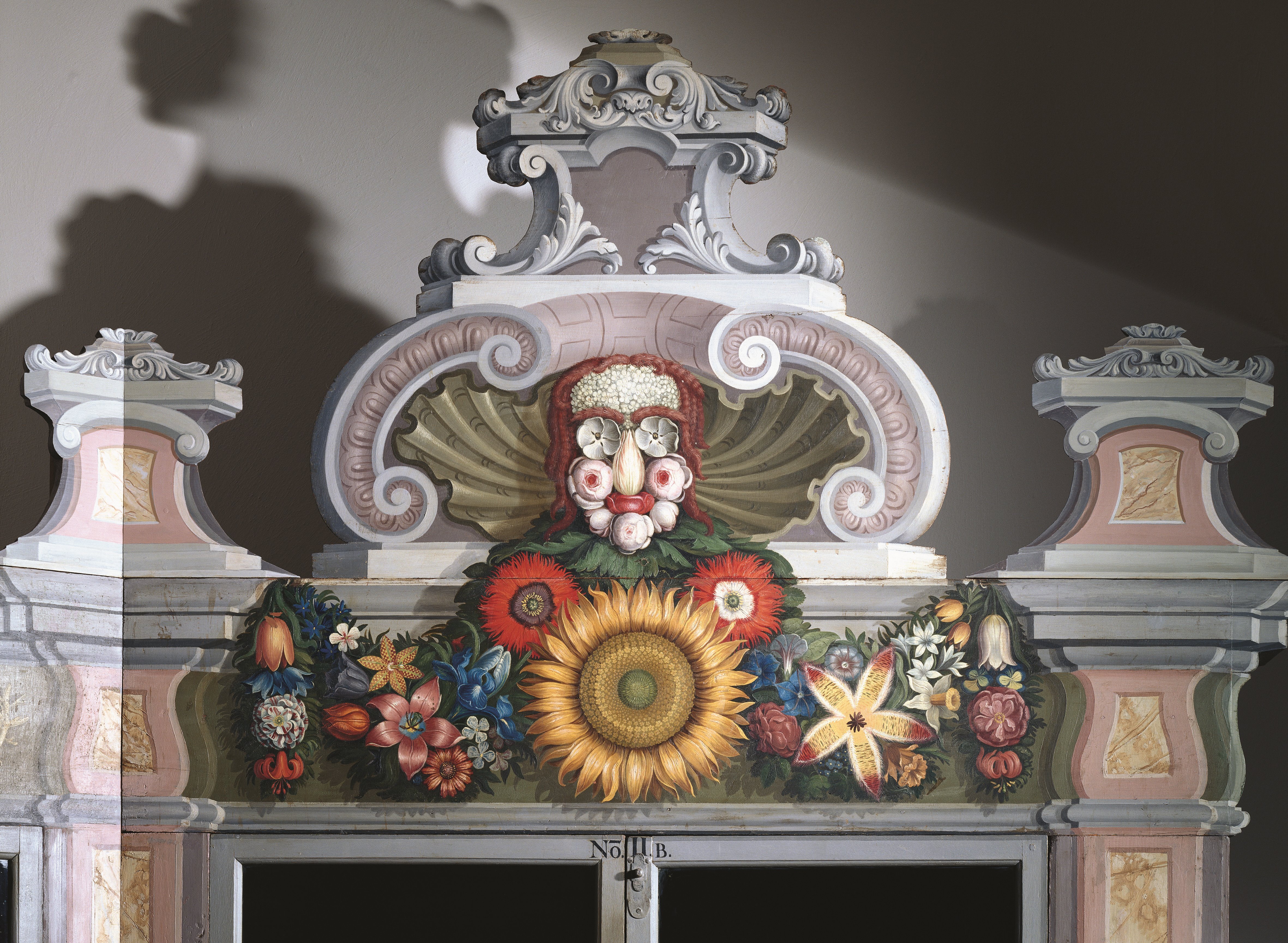 Ein nachgebauter Giebel mit geschwungenen Formen und fantasievollen bunten Blumenranken lassen ein Gesicht daraus im Zentrum des Komplexes entstehen.