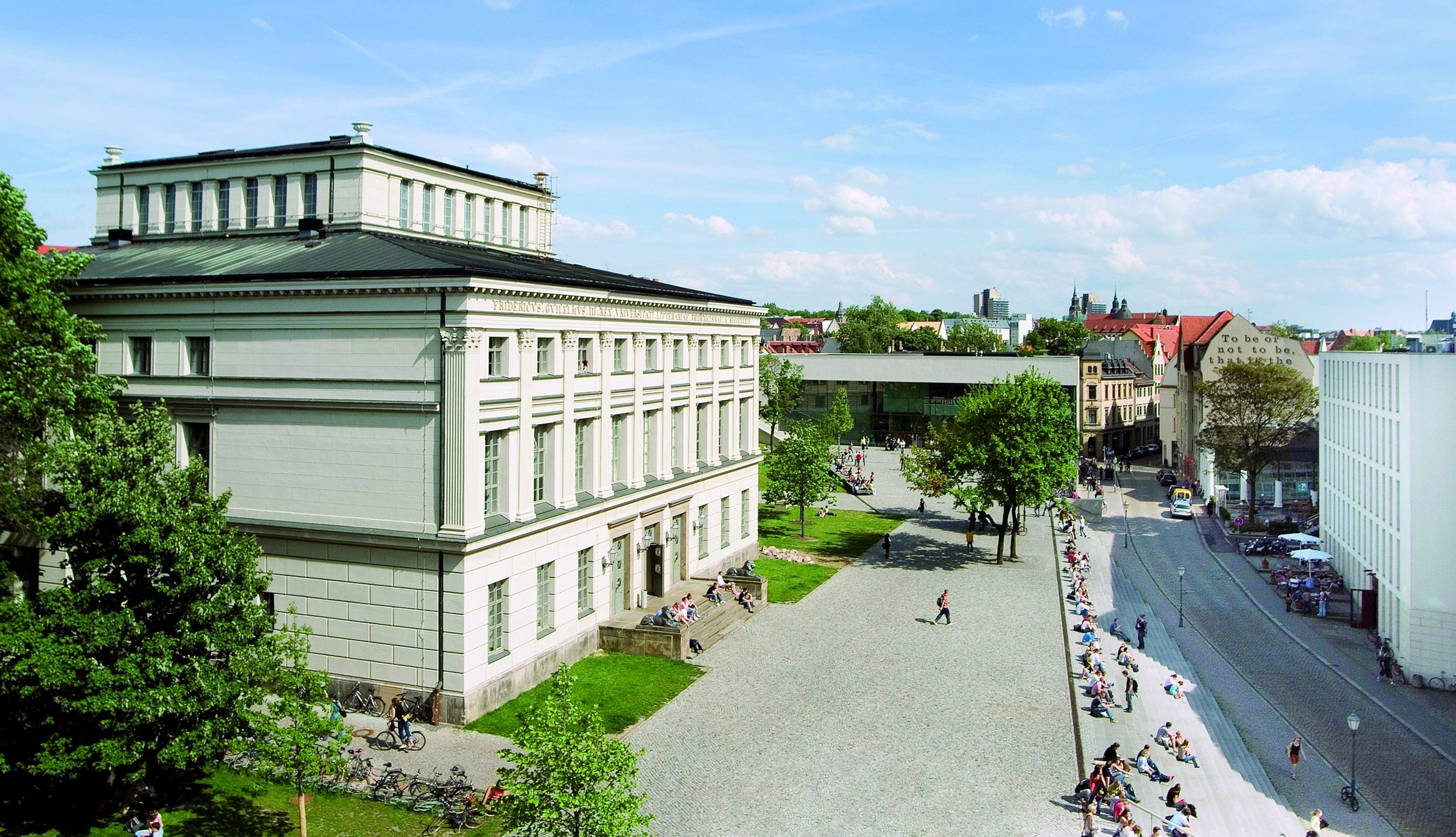 Das Löwengebäude der Martin-Luther-Universität Halle-Wittenberg beherbergt die Zentrale Kustodie und das Universitätsmuseum. das dreigeschossige helle Gebäude steht auf einem großen Platz umringt von grünen Bäumen. Gegenüber steht das Juridicum.