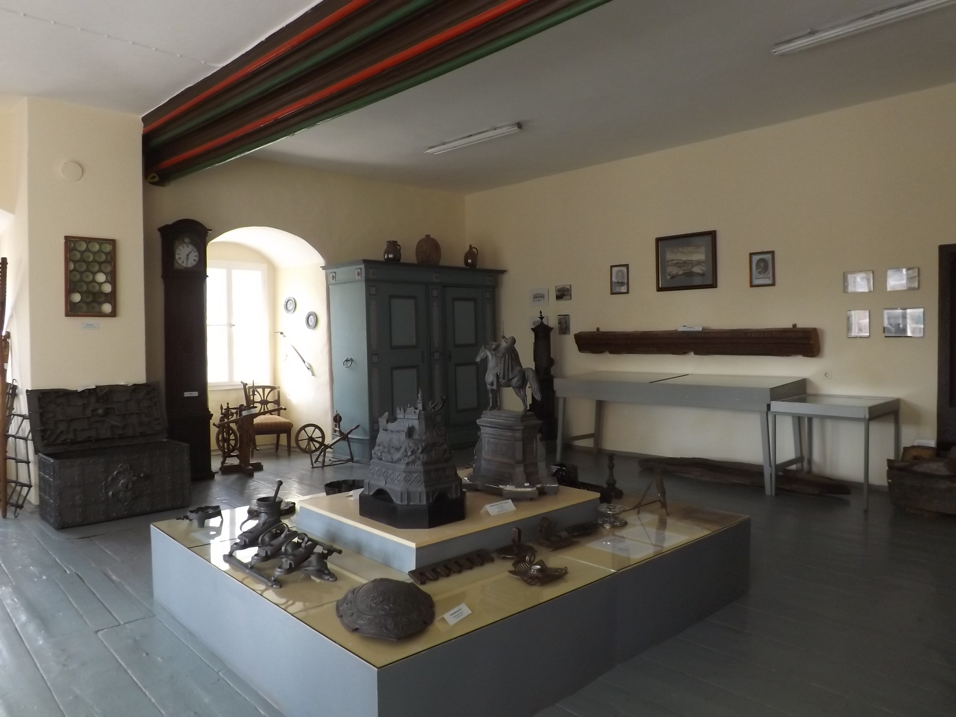 Im Ausstellungsrau werden auf einem Plateau in der Mitte Modelle eines Reiterstandbildes und einer Burg gezeigt. Ein Schild, eine Tierfalle und weitere Objekte umgeben die Modelle. Im Raum stehen zudem noch eine große Eisentruhe, eine Standuhr und ein Schrank.