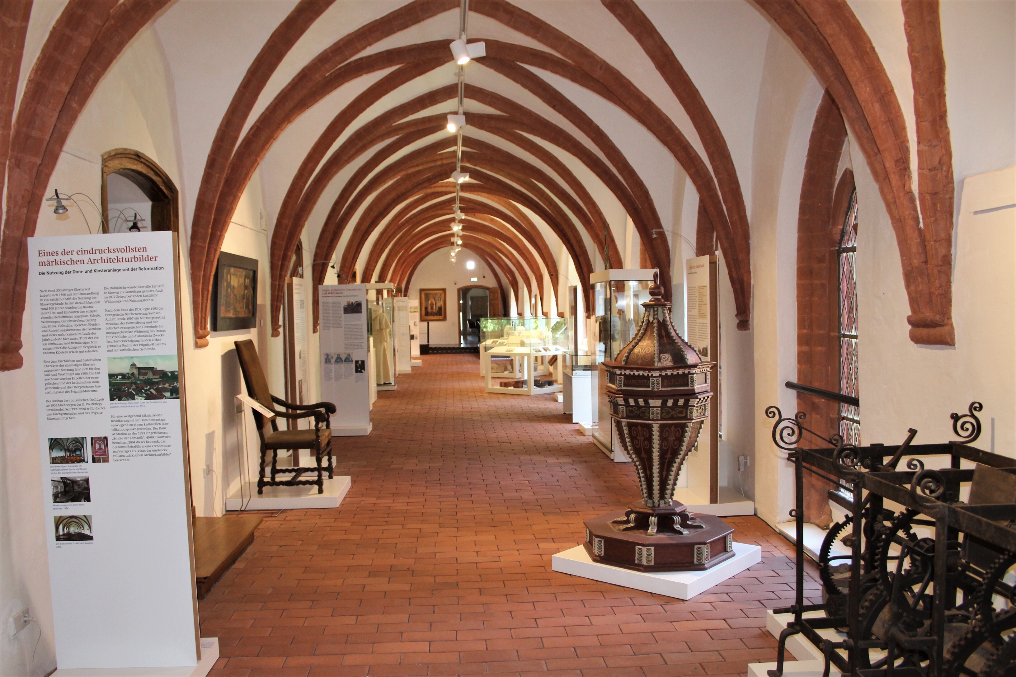 Der Kreuzgang des Havelberger Domes besitzt rote Gewölberippen und einen Boden aus rotem Stein. Hier stehen verschiedene Ausstellungsobjekte teilweise in Vitrinen. Mehrere Aufsteller geben zusätzliche Informationen.