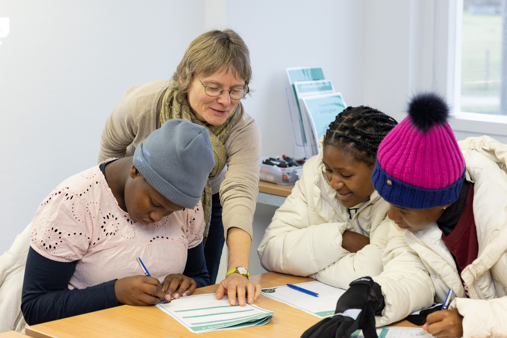 Projekttage in der Gedenkstätte. Drei Frauen sitzen an einem Tisch und bearbeiten eine Aufgabe auf einem Blatt Papier. Eine weitere Frau steht dahinter und hilft den drei anderen Frauen.