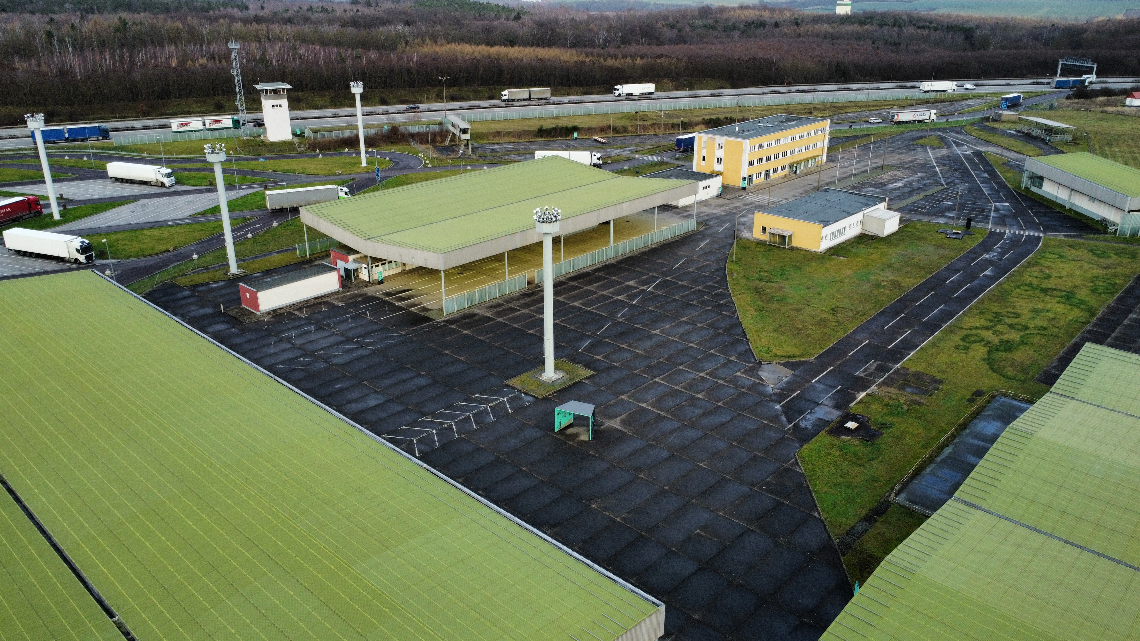 Drohnenaufnahme vom Gelände der Gedenkstätte. Grüne Dächer und Rasenflächen wechseln sich mit grauen Platten auf dem Gelände ab. Einzelne Masten ragen in die Höhe.
