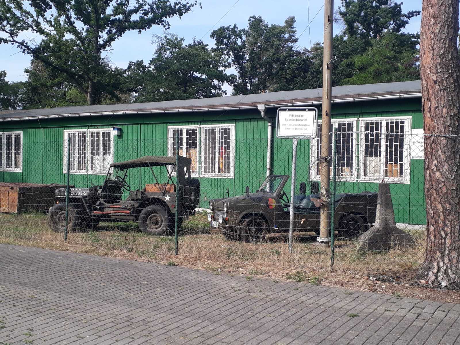 Der Haupteingang zum Militärhistorischen Museum. Hinter einem Zaun stehen militärische Fahrzeuge auf einer Wiese. Die Kaserne dahinter ist grün und besitzt weiße Fensterrahmen.