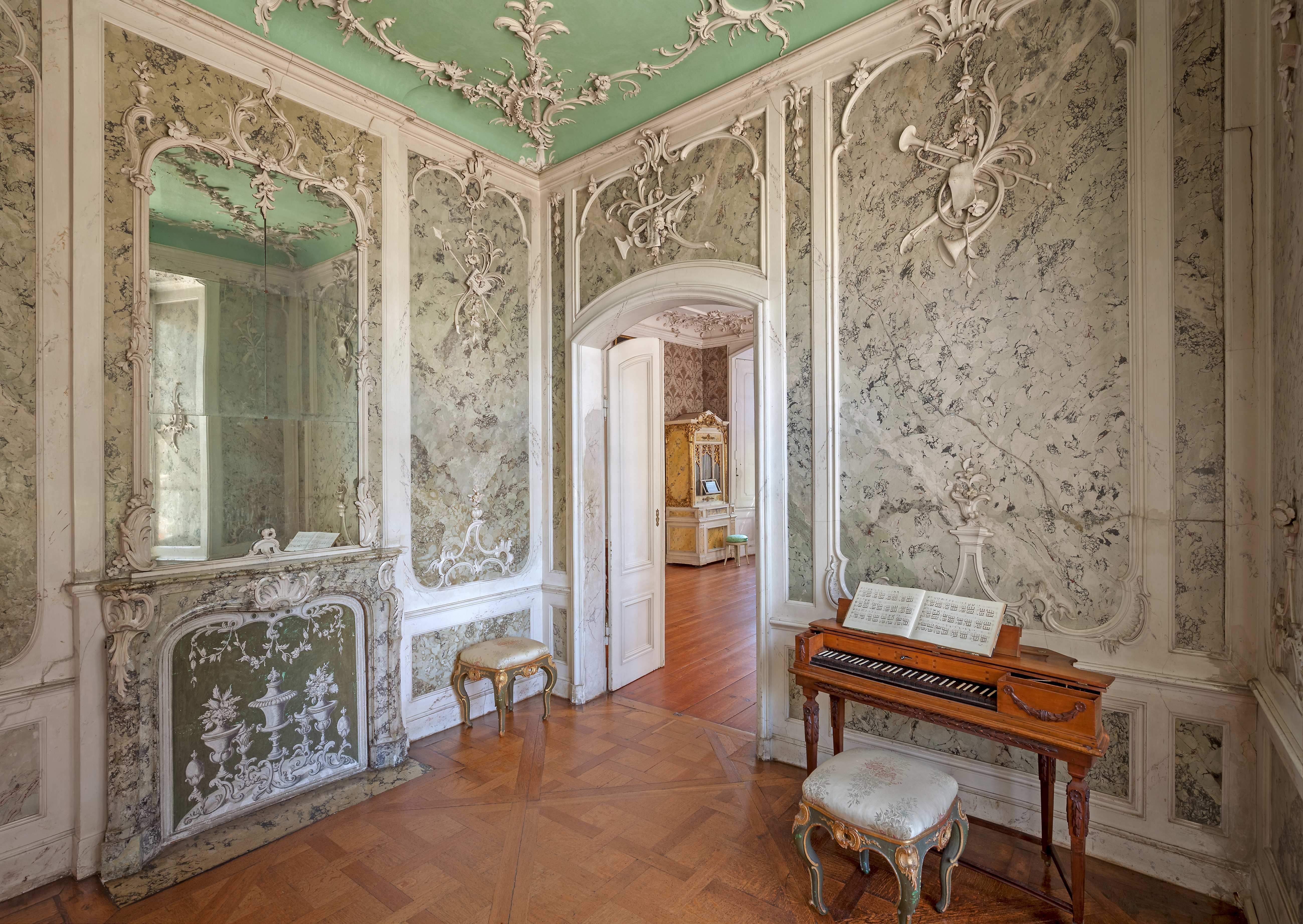 Das Musikkabinett im Schloss Mosigkau. Die Wände bestehen aus hellem Marmor und sind ebenso wie die Decke geschmückt mit Stuck. Vor einer Wand steht ein Tafelklavier aus Holz.