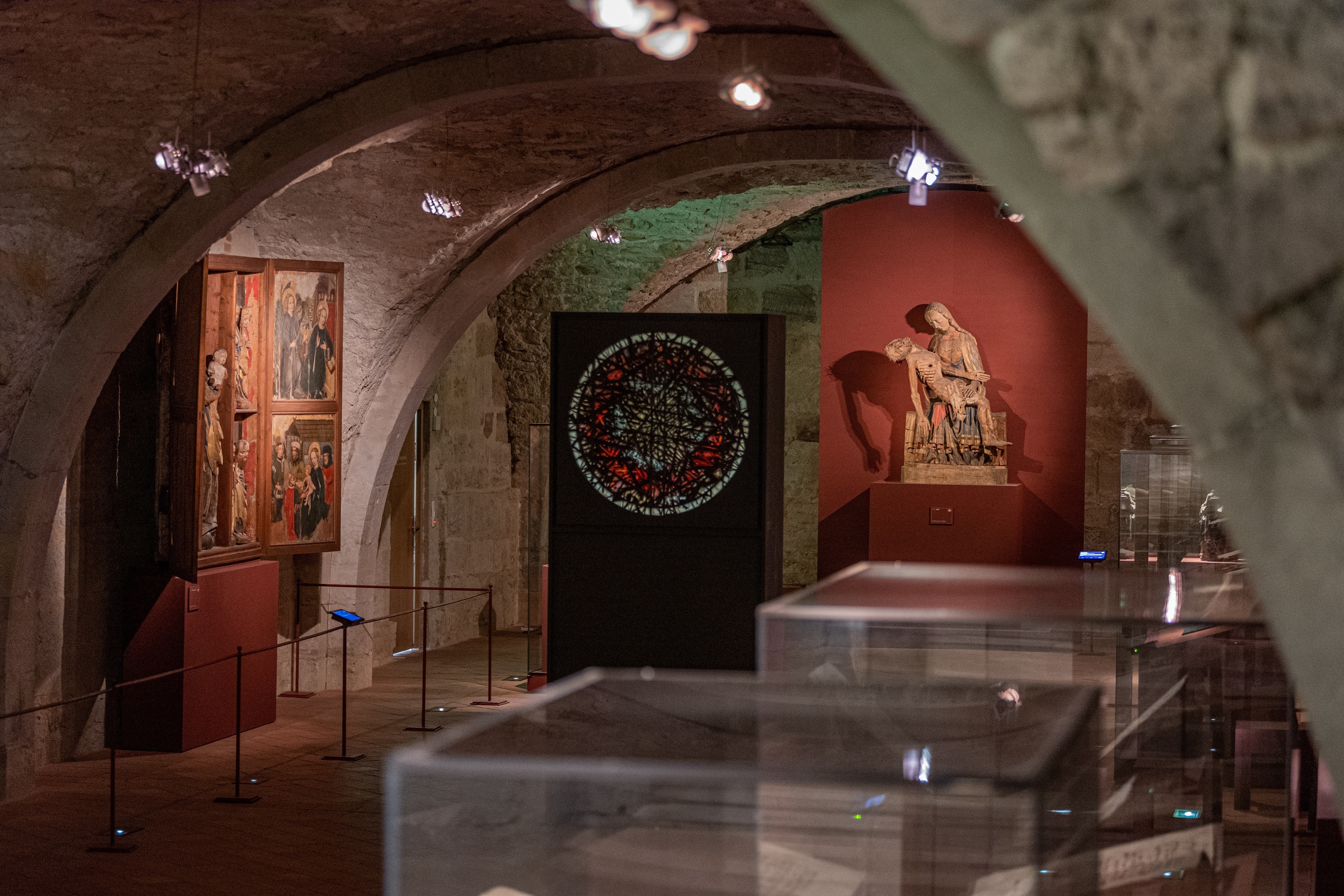 Das Naumburger Domschatzgewölbe. Ein Flügelaltar mit Holzfiguren, ein rundes Buntglasfenster und die Naumburger Pieta werden im Gewölbe präsentiert.