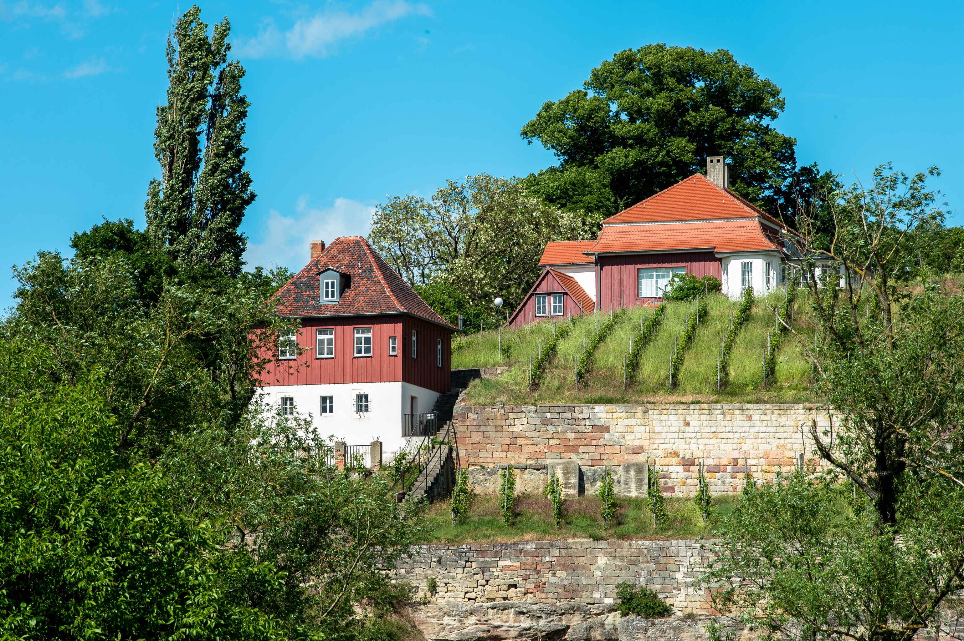 Das Radierstübchen und das Max Klinger Haus liegen versteckt zwischen den Weinbergen. Das Radierstübchen liegt vor dem Haus. Das untere Geschoss besitzt eine weiße Fassade und das obere trägt eine rote Holzverkleidung.