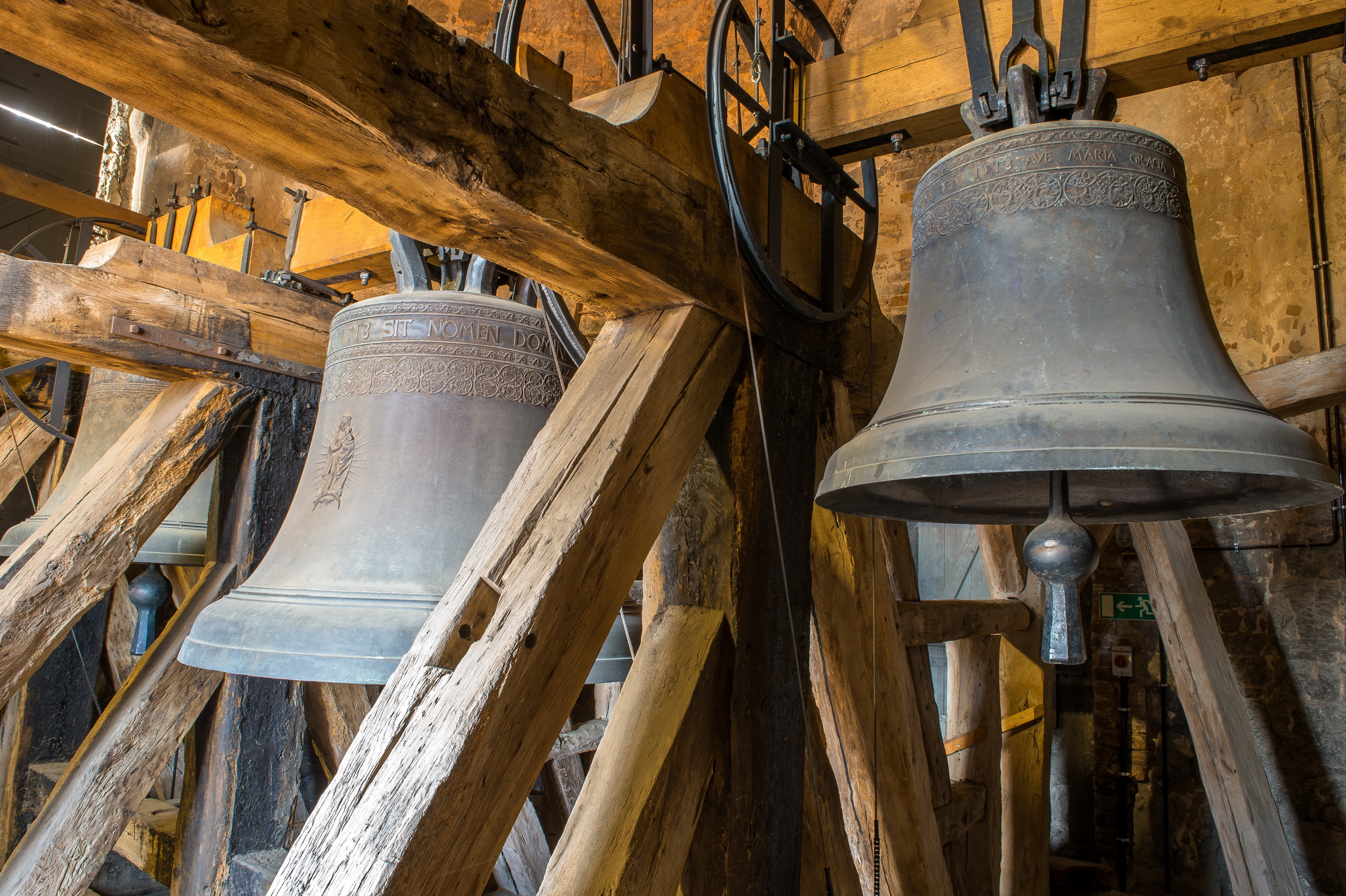 Im Glockenstuhl sind drei unterschiedlich große Glocken erkennbar. Holzbalkenkonstruktionen dienen als Vorrichtungen zum Schwingen der Glocken.