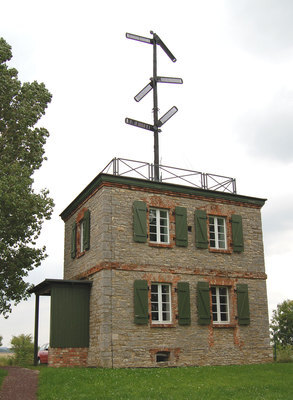Das Telegrafiemuseum von Außen. Ein graues Gebäude aus Stein mit grünen Fensterläden und auf dem Dach steht ein optischer Signalmast mit sechs Telegrafenarmen.