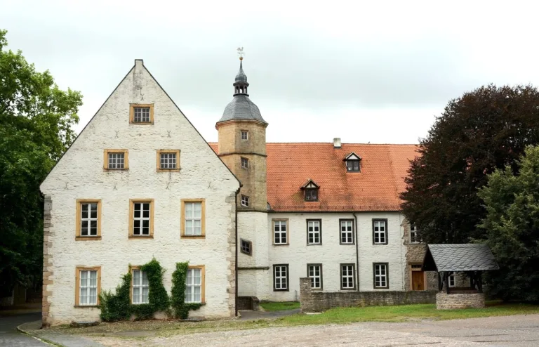 Novalis Schloss Oberwiederstedt. Eine weiße Schlossanlage mit einem kleinen Treppenturm und einem Brunnen vor dem Hauptgebäude.