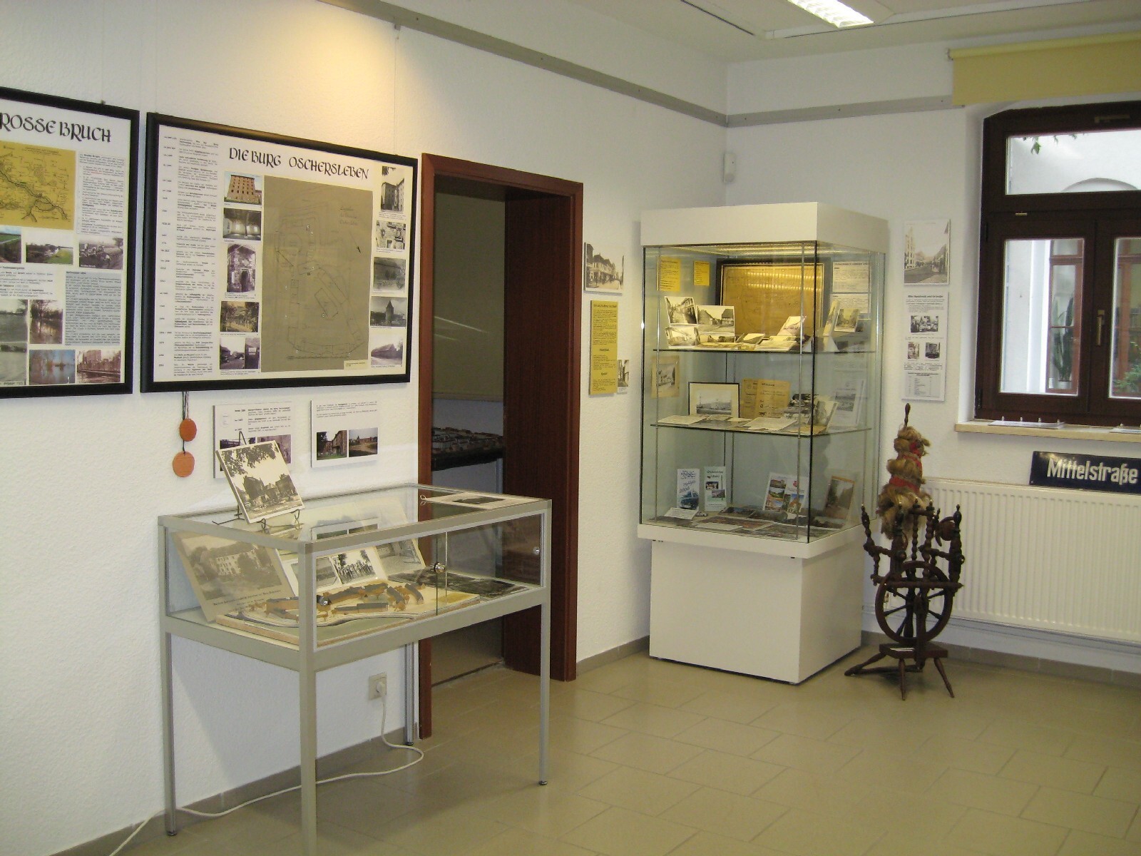 Die Ausstellung "Von Oscherslevo bis Oschersleben" zeigt ein altes Spinnrad und verkleinerte Stadtmodelle, welche mit Fotografien untermauert werden.