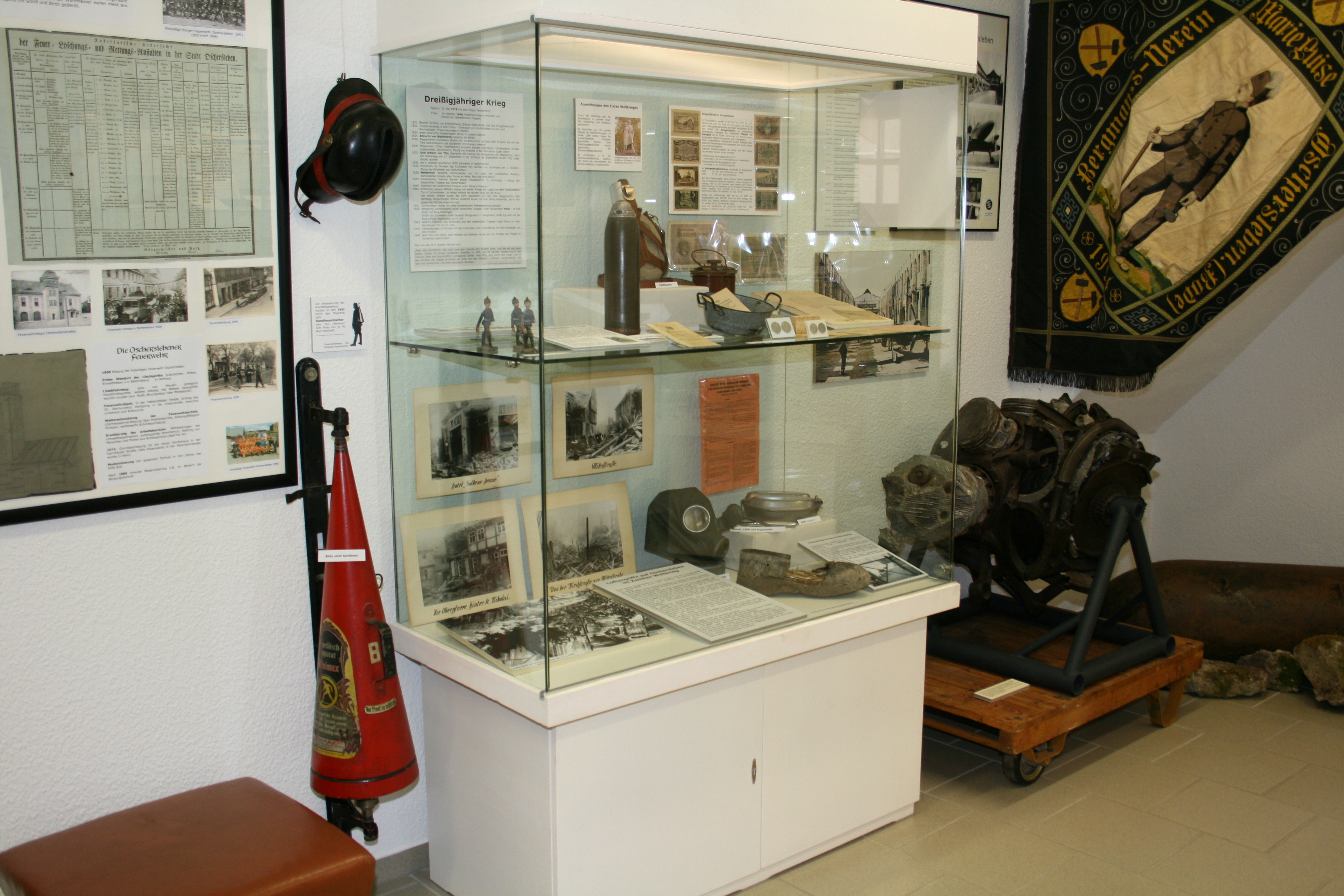 Ausstellung "Von Oscherslevo bis Oschersleben". In einer Vitrine werden Fotografien, eine Gasmaske und kleine Zinnsoldaten gezeigt. Im Hintergrund hängt eine Flagge des Bergmanns-Vereins.