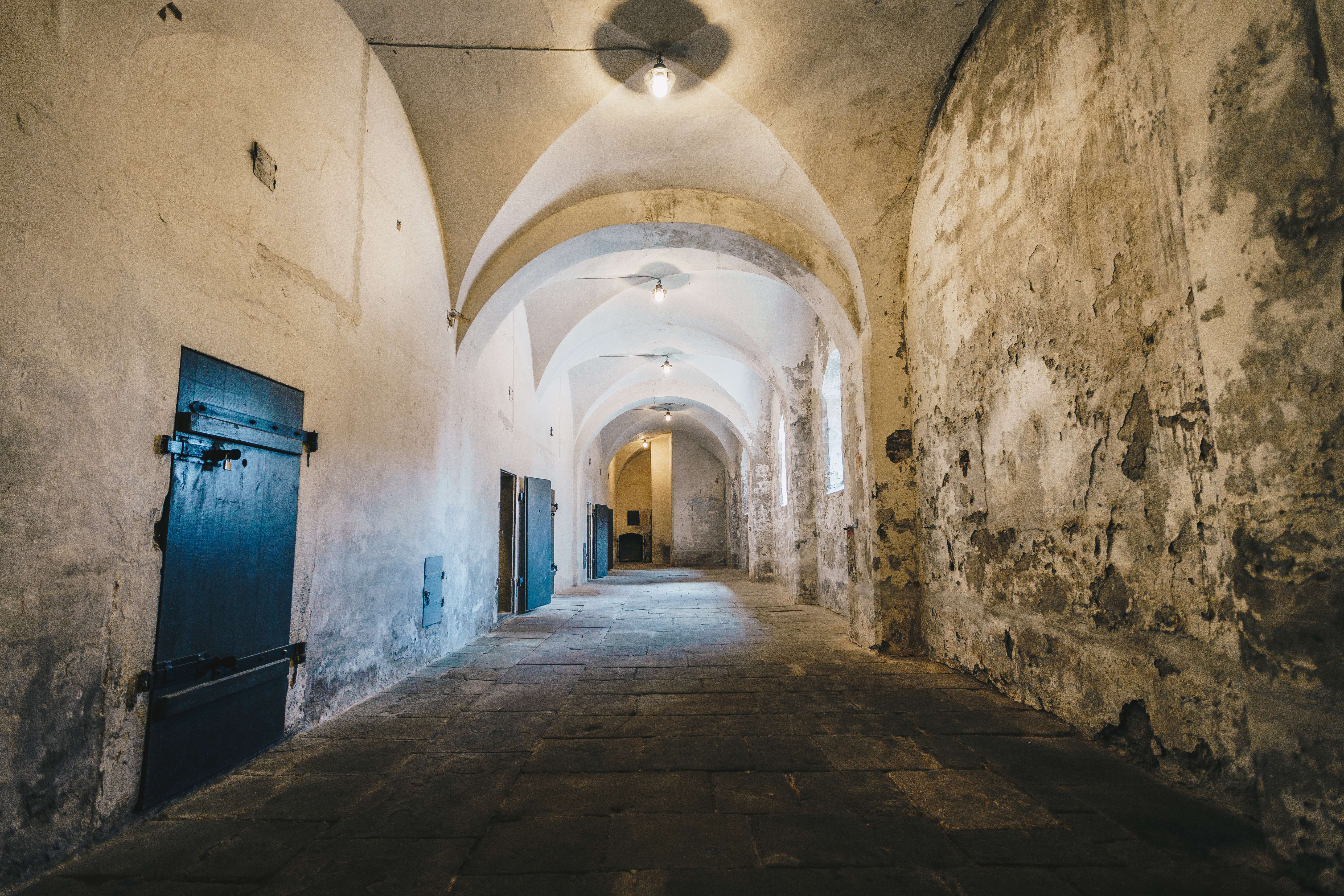 Der ehemalige Strafbunker. Ein Durchgang mit verschmutzten weißen Wänden, einer Gewölbedecke und schwarzen Holztüren.
