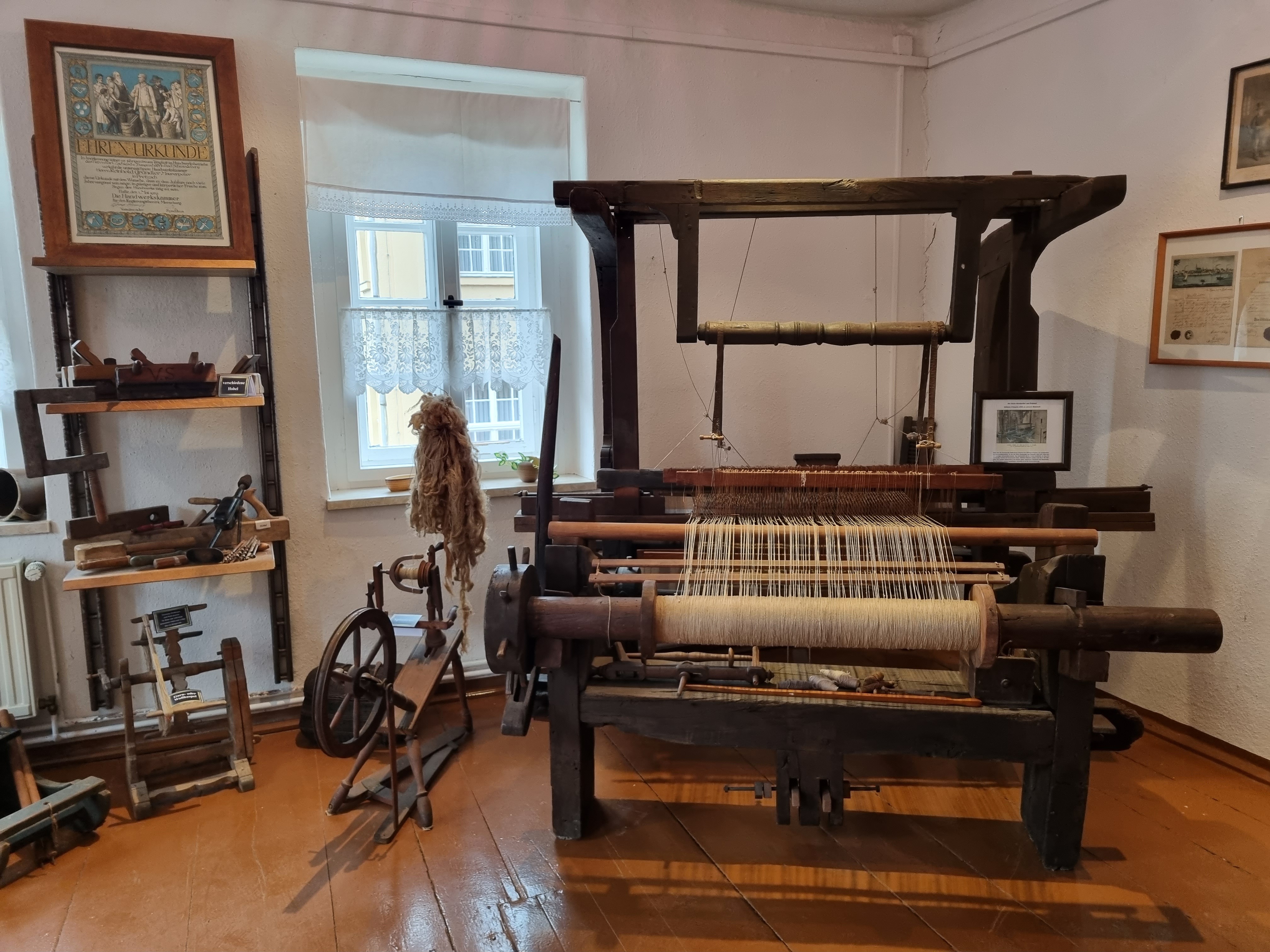 Handwebstuhl aus dem Heimatmuseum Pretzsch Elbe. In den Webstuhl wurden weiße Fäden eingespannt. Daneben steht ein Spinnrad.
