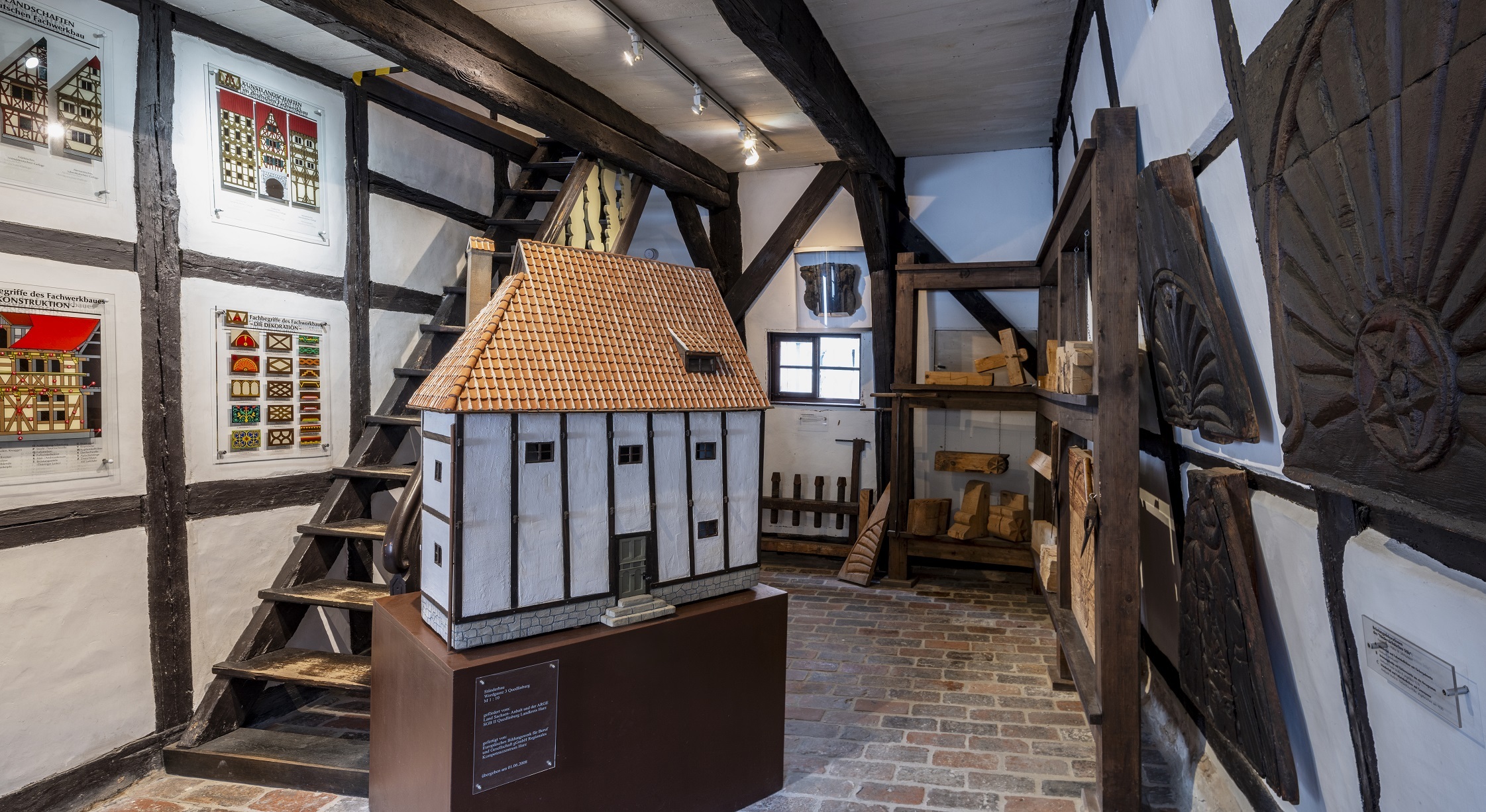 In der Mitte des Ausstellungsraumes des Fachwerksmuseums steht ein Modell des Ständerbaus. An den Wänden hängen Grafiken zum Fachwerkbau und ornamentierte Holzplatten.
