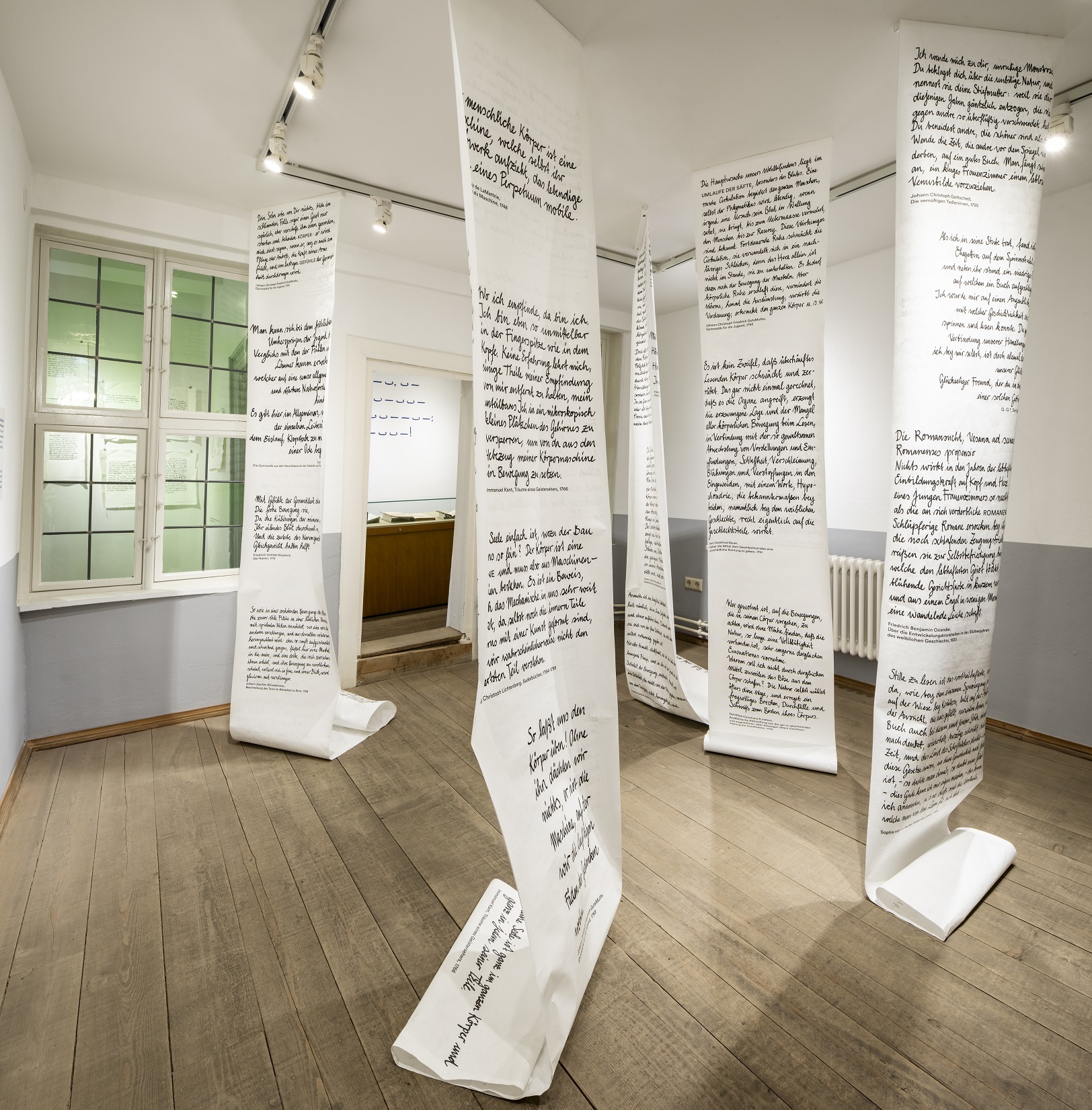 Ausstellung im Klopstockhaus. Von der Decke hängen lange Banner, die bis auf den Boden reichen und mit kurzen Texten bedruckt sind.