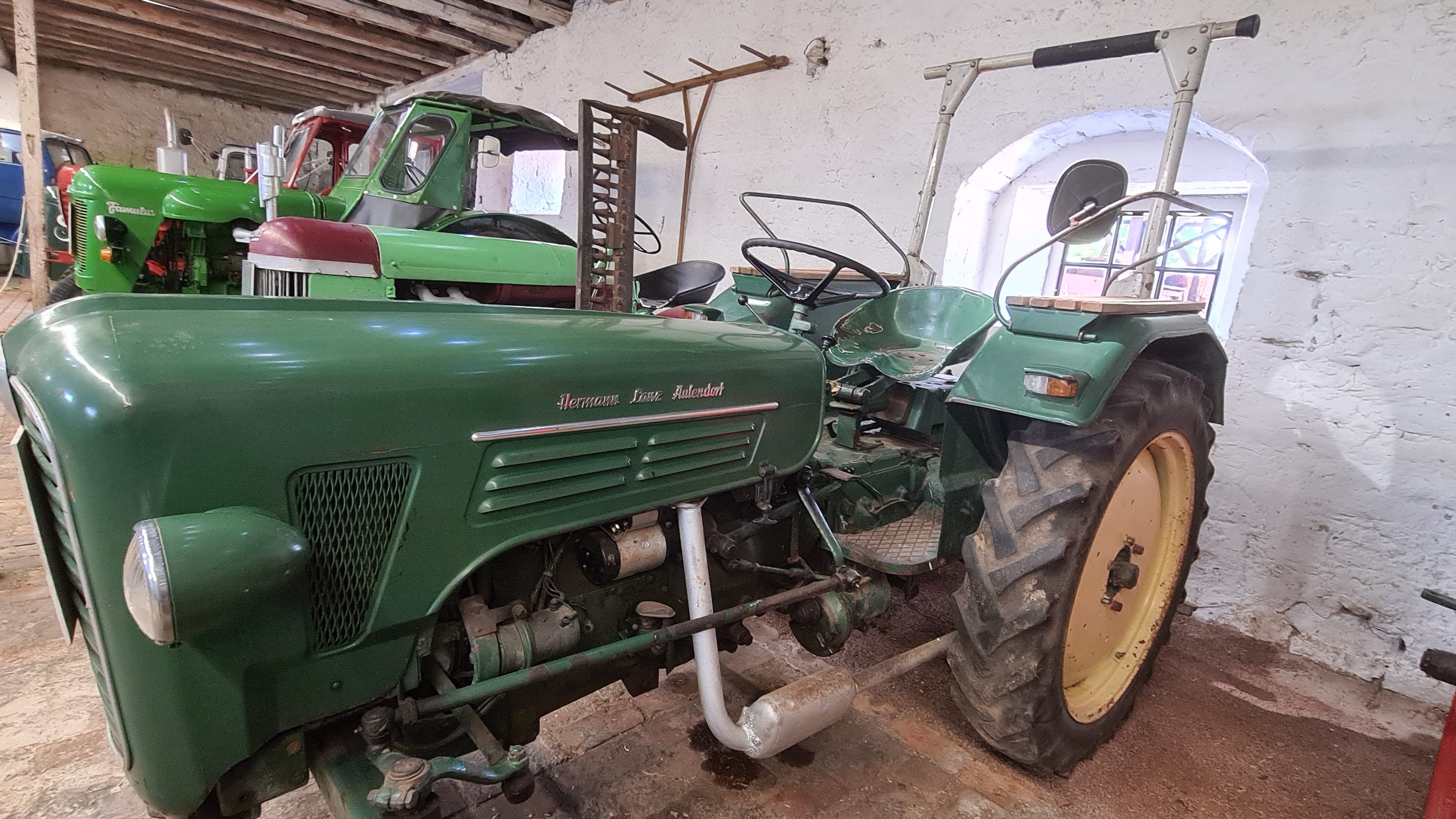 Eine Reihe von grünen Traktoren unterschiedlicher Modelle steht in einer Scheune.