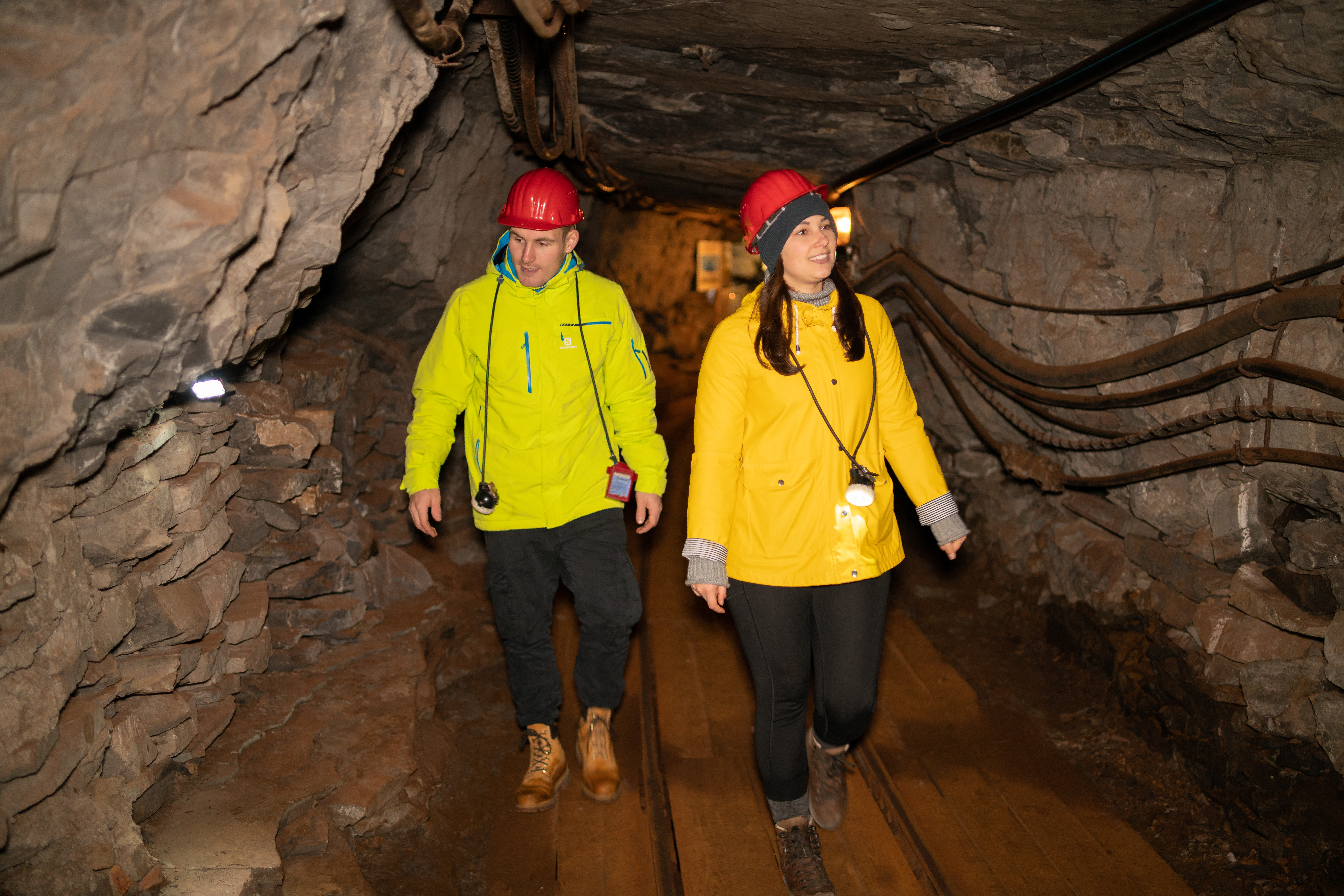 Zwei Personen mit gelben Jacken und roten Helmen laufen durch einen Schacht im Erlebnisbergwerk.