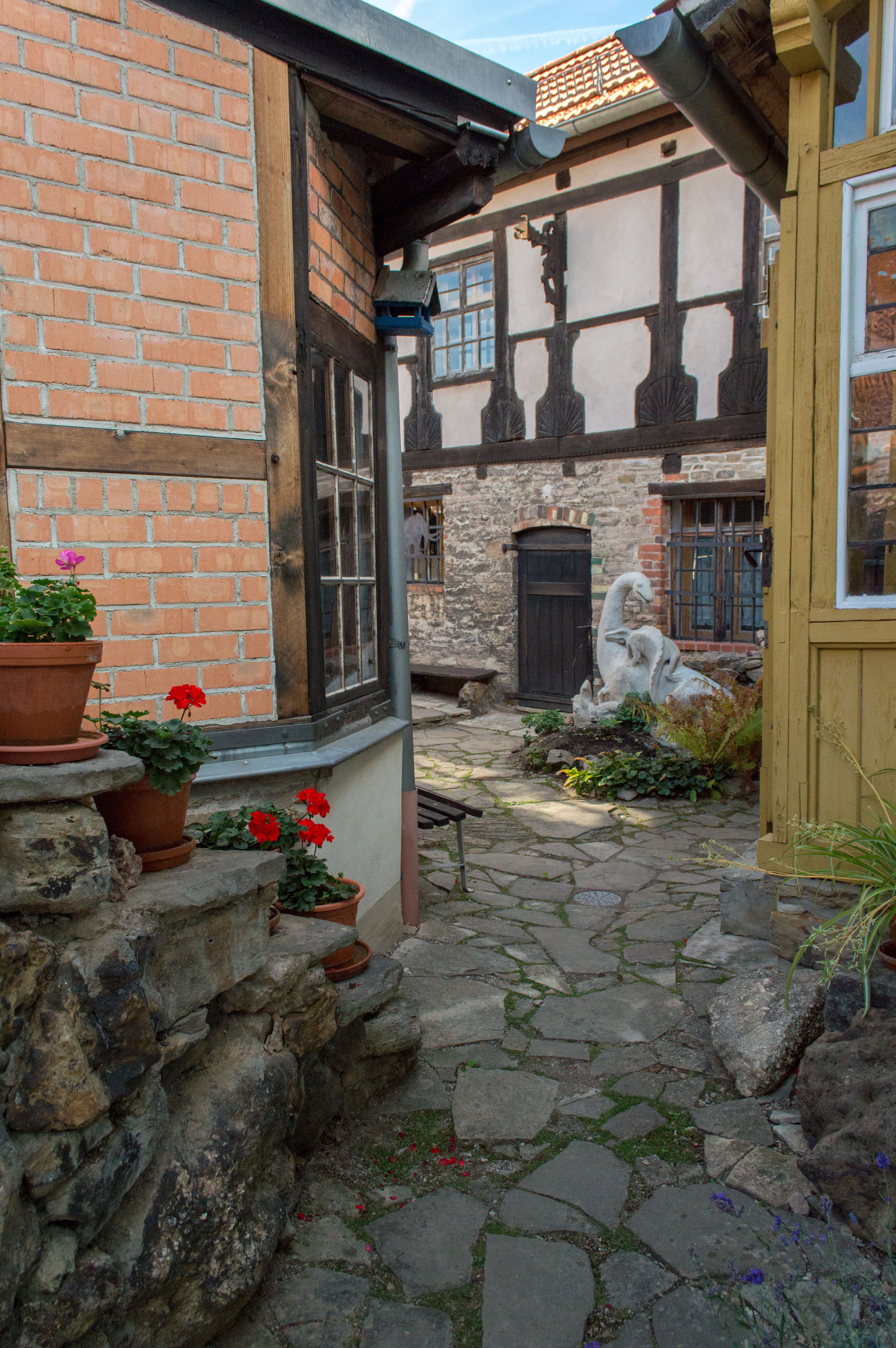 Das Spengler-Haus: Blick durch den Hof auf eine Dinosaurier Skulptur. Auf der linken Seite stehen rote Blumen auf einer Steintreppe.