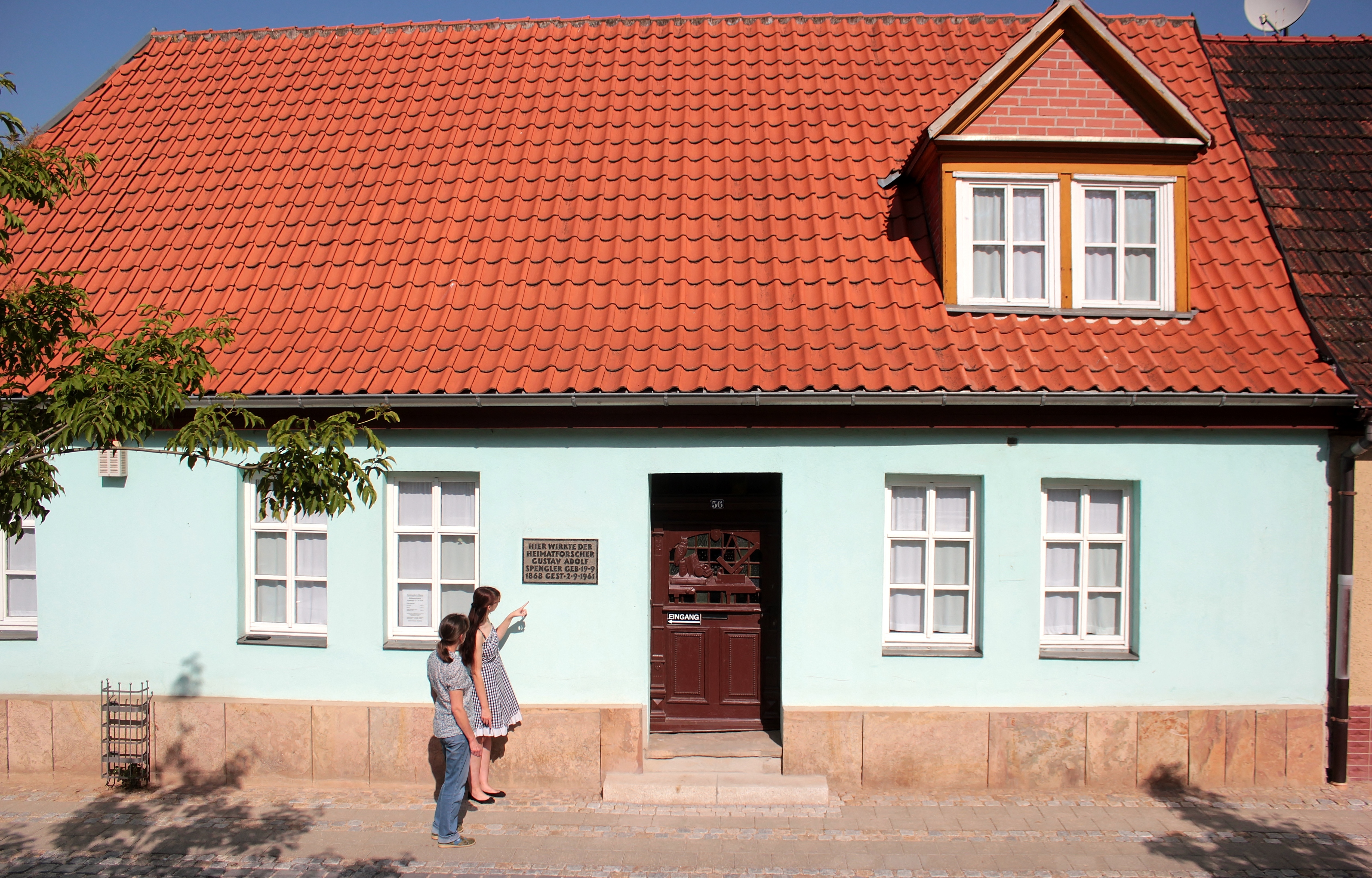 Das Spengler-Haus besitzt eine hellblaue Fassade, weiße Fensterrahmen und ein rotes Ziegeldach.