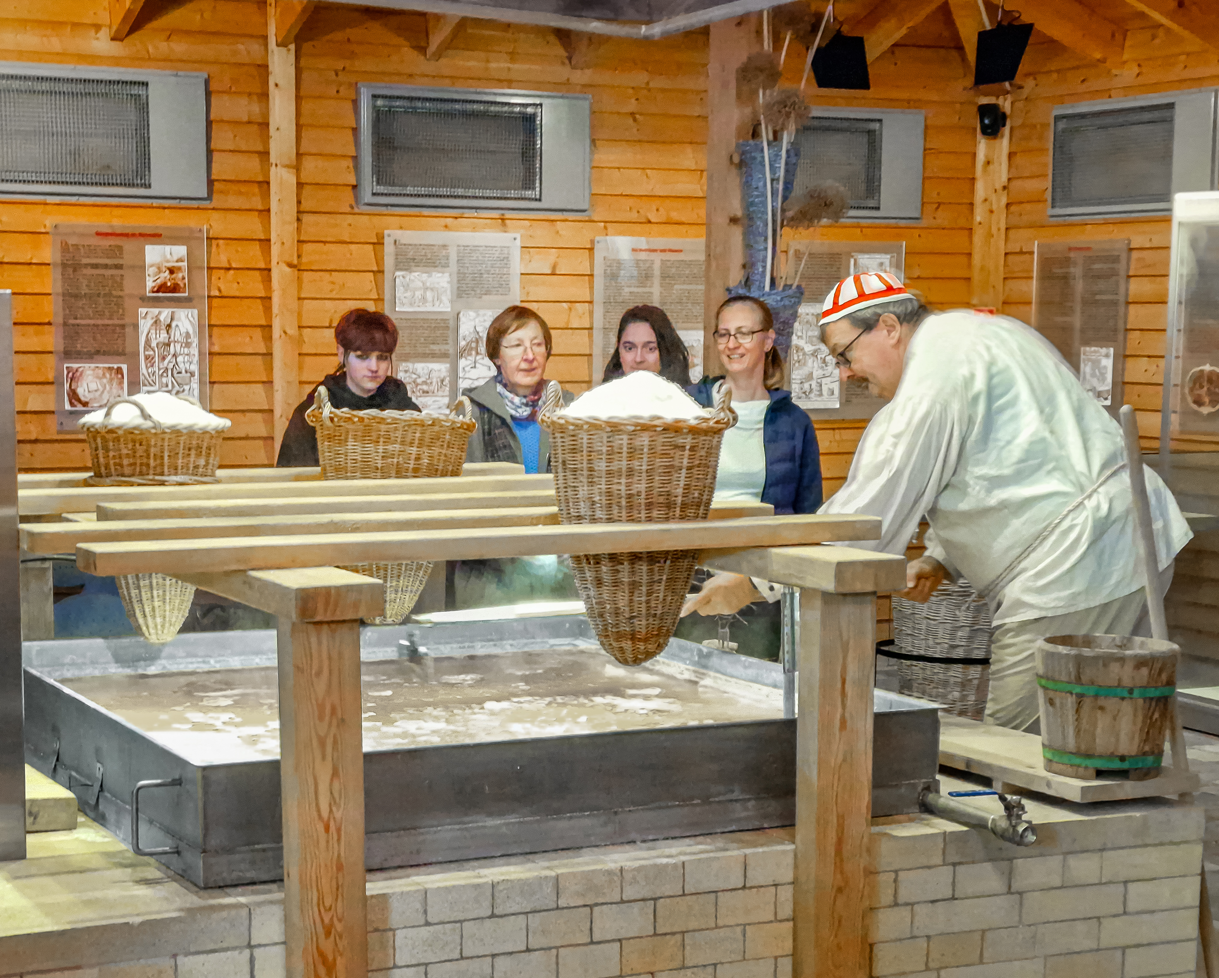 Schausieden. Ein Mann demonstriert das Salzsieden. Über einem Behälter mit Wasser stecken Körbe mit Salz zwischen Holzleisten.