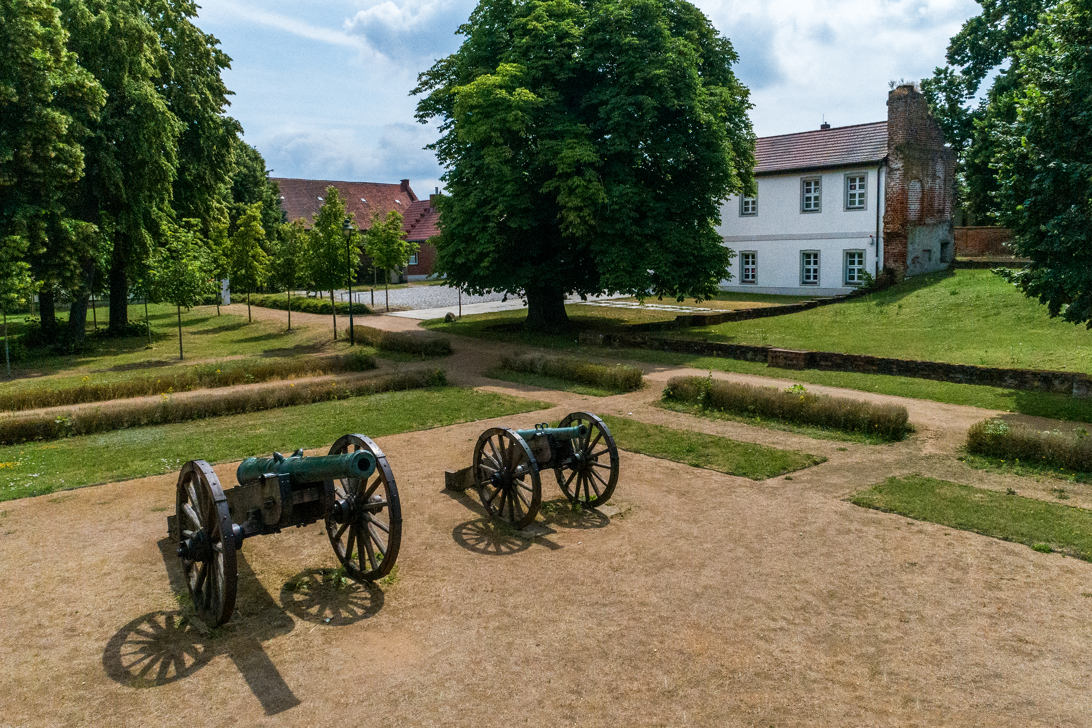 Auf einer hellen Rasenfläche stehen zwei Kanonen auf Rädern. Im Hintergrund breitet sich eine Parklandschaft sowie die weißen Gebäude des Bismarcks-Museum aus.